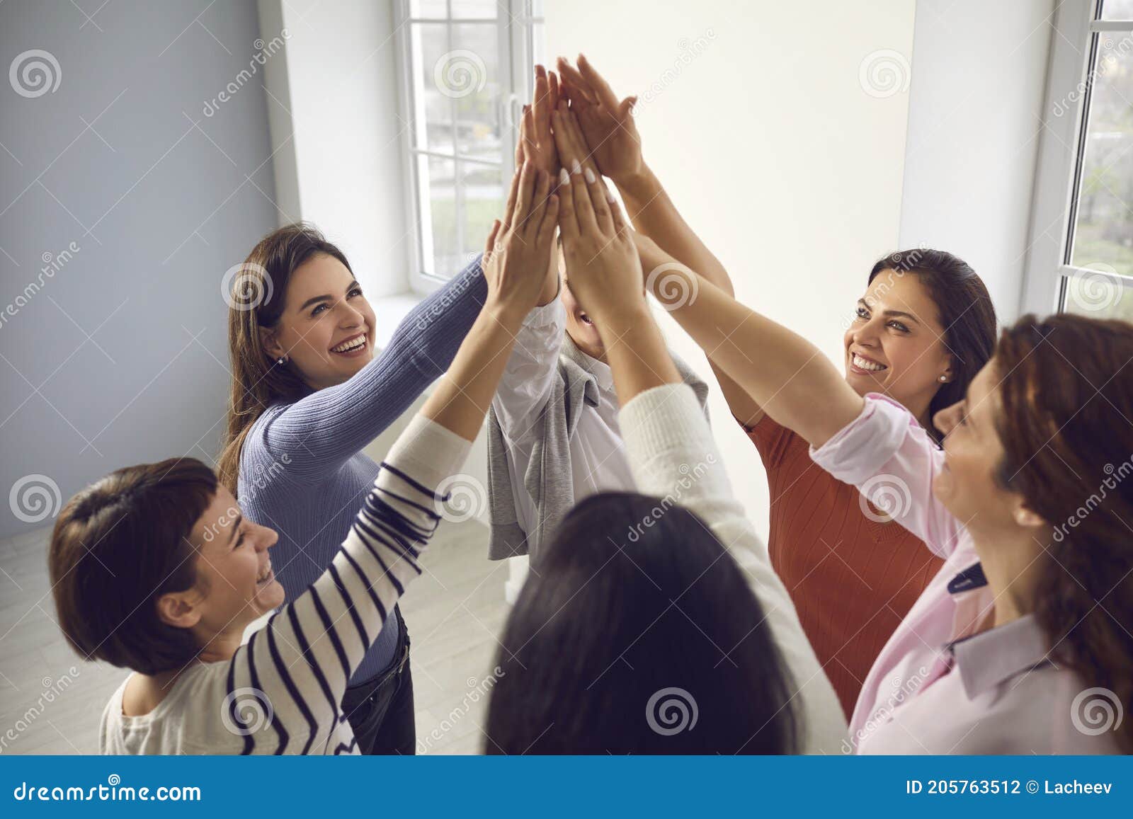 team of happy young women joining hands, feeling united, confident and empowered