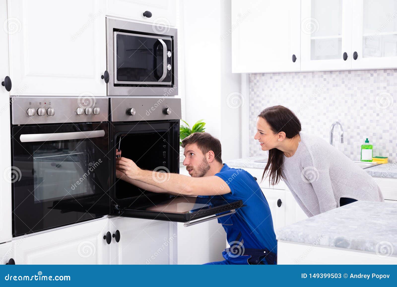 technician in overall fixing oven in kitchen