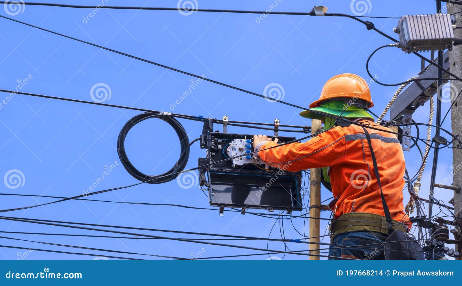technician on wooden ladder is working to install fiber optic and splitter box on power pole against blue sky