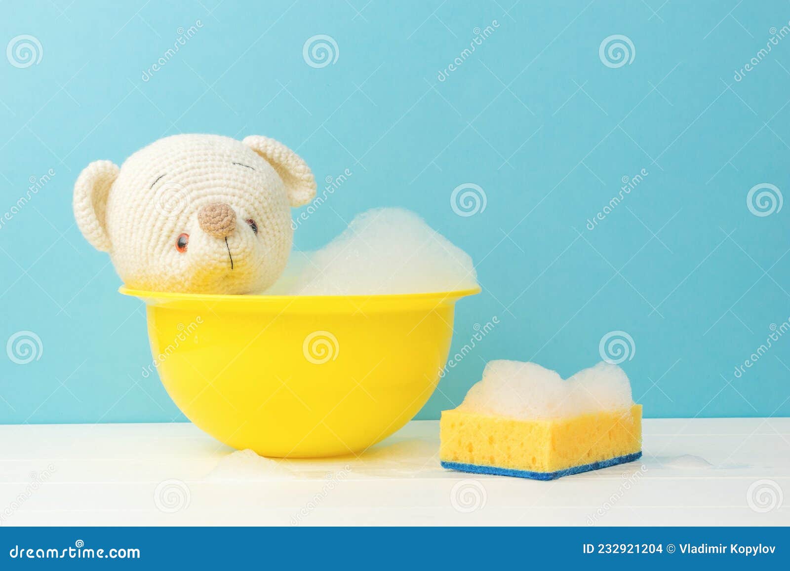 A Teddy Bear in a Basin with Foam and a Foam Sponge on a White Table