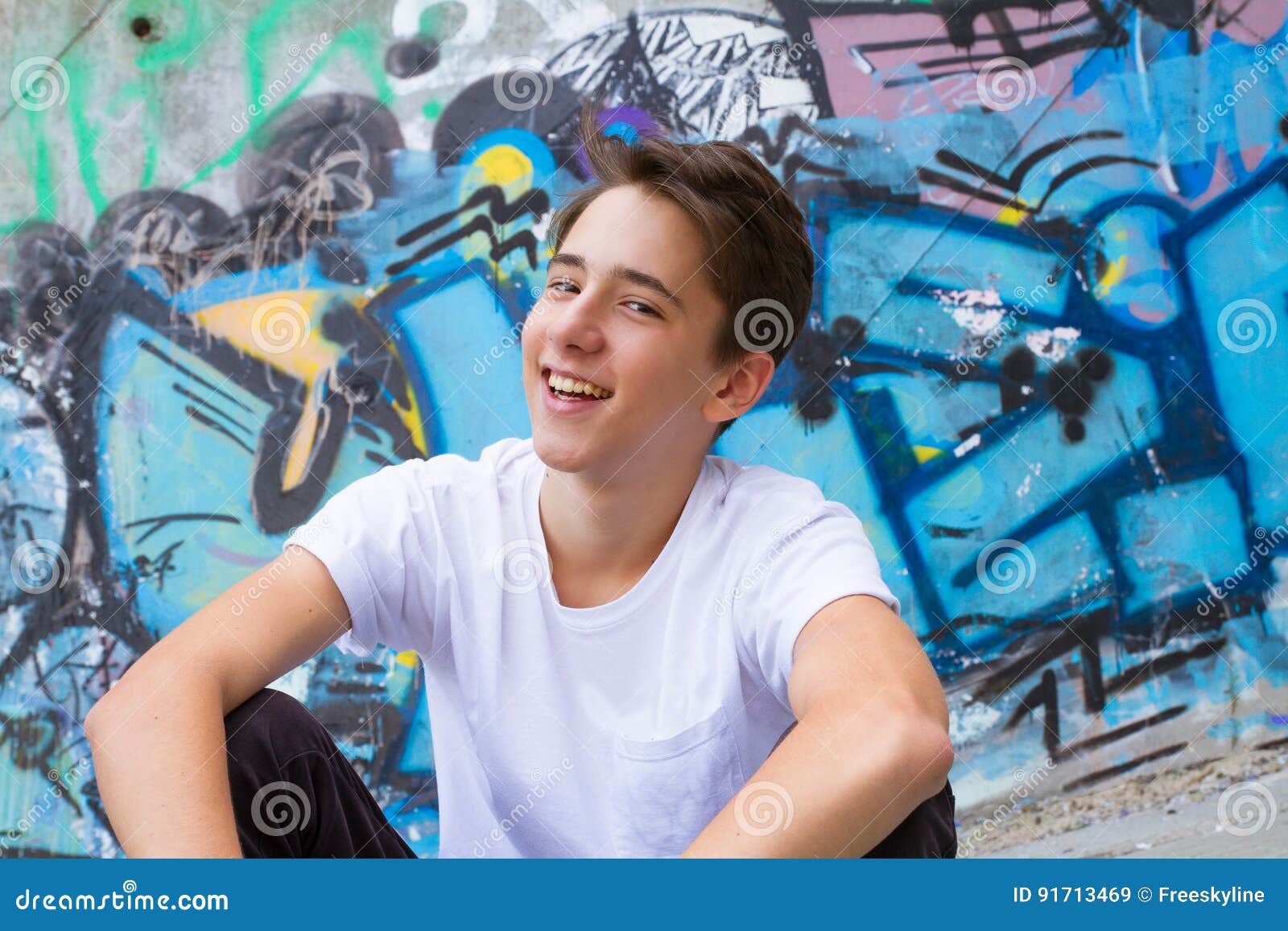 Teen boy in blue shirt. Outside portrait of teen boy. Smiling Handsome teenager next to graffiti painted wall