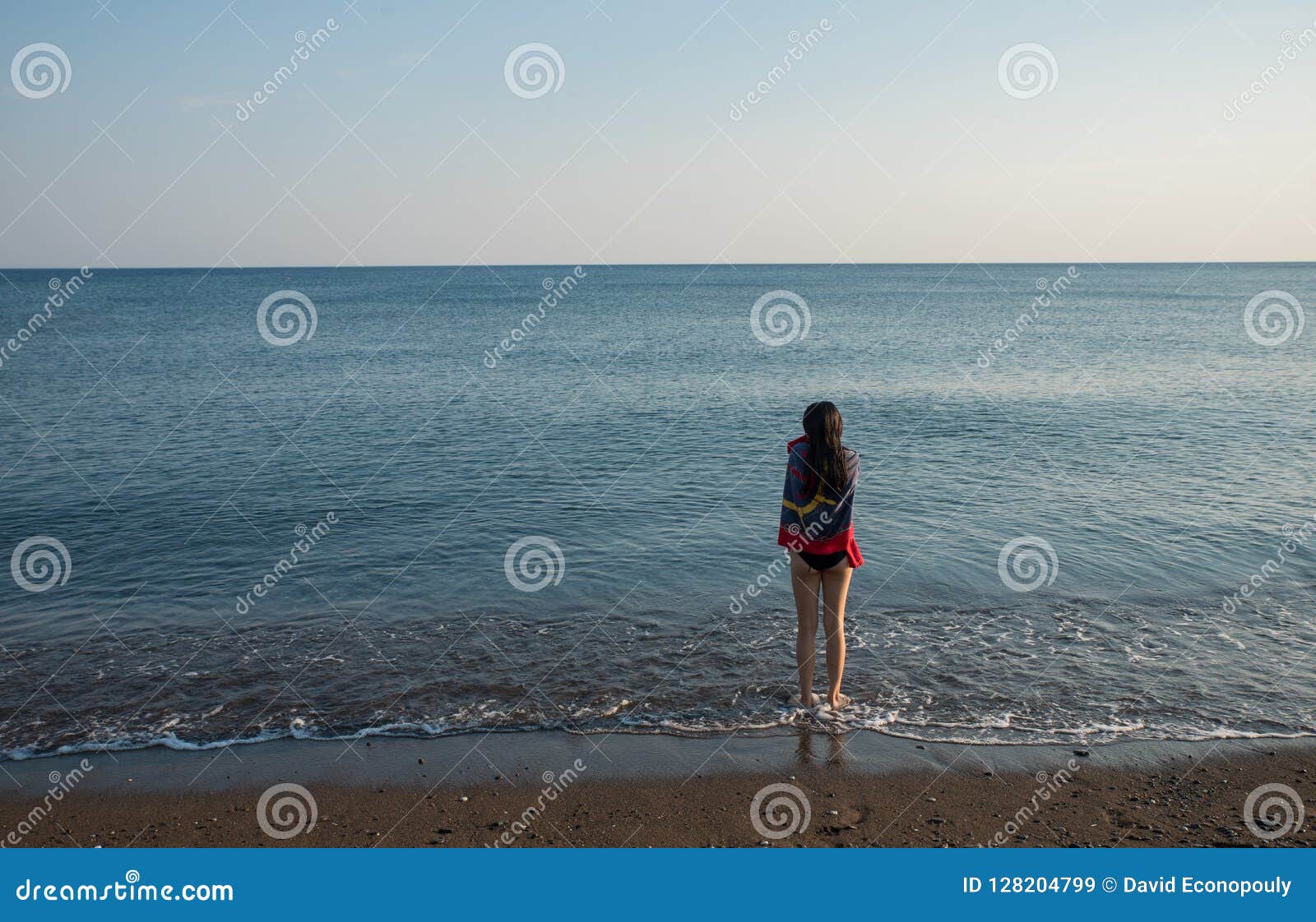 teen standing at water`s edge with towel looking out to sea