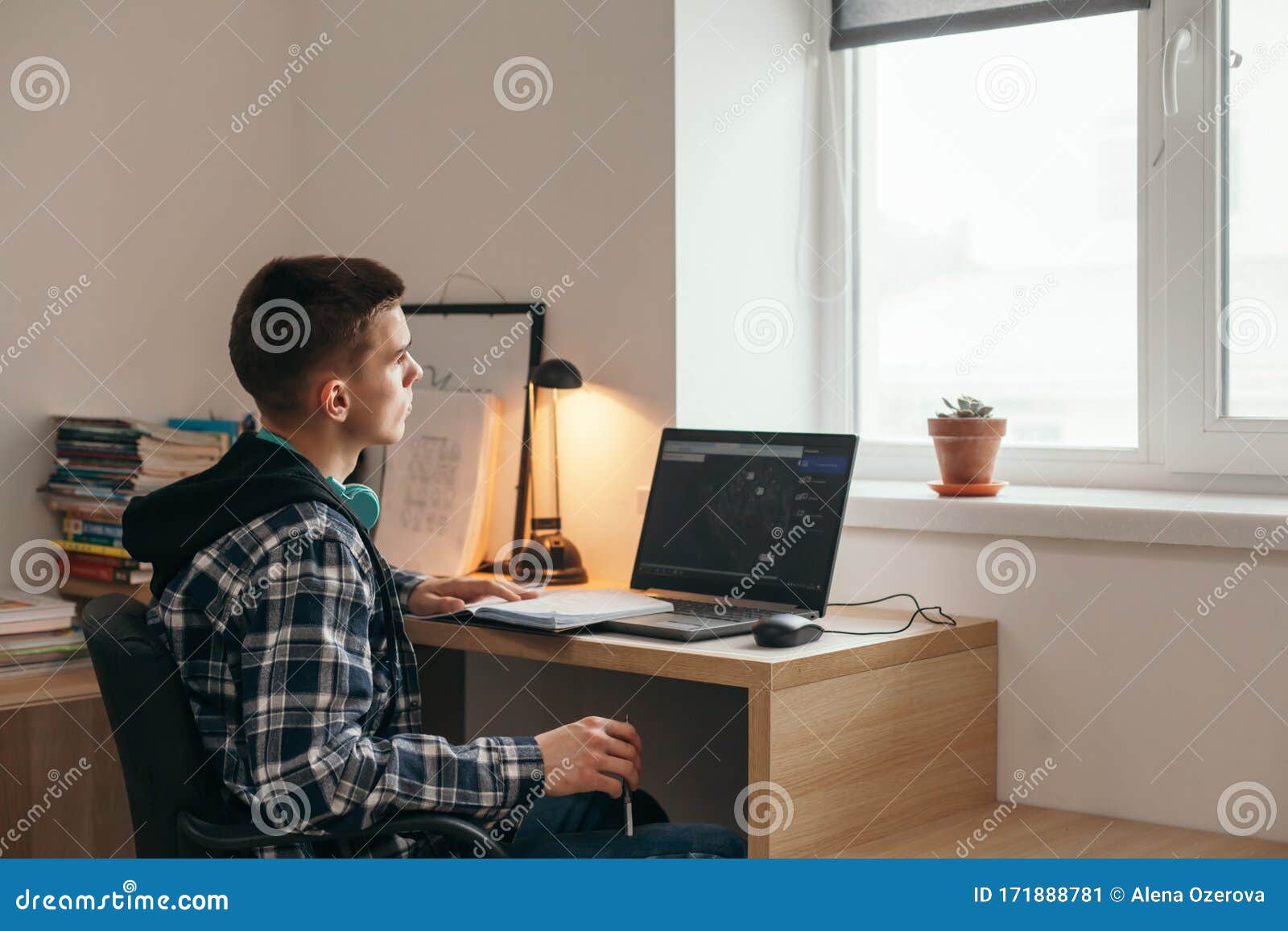Teenage Boy Doing Homework Using Computer Sitting By Desk In Room