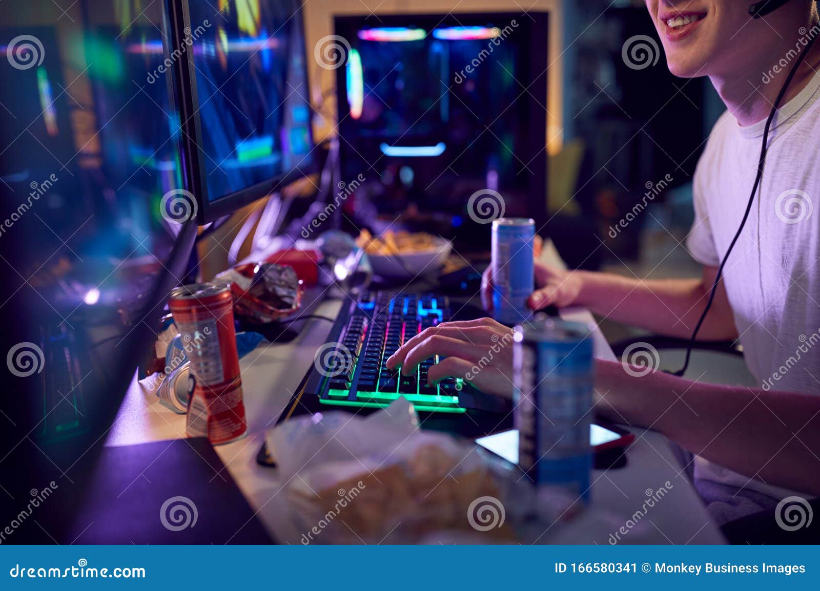 teenage boy drinking caffeine energy drink gaming at home using dual computer screens at night