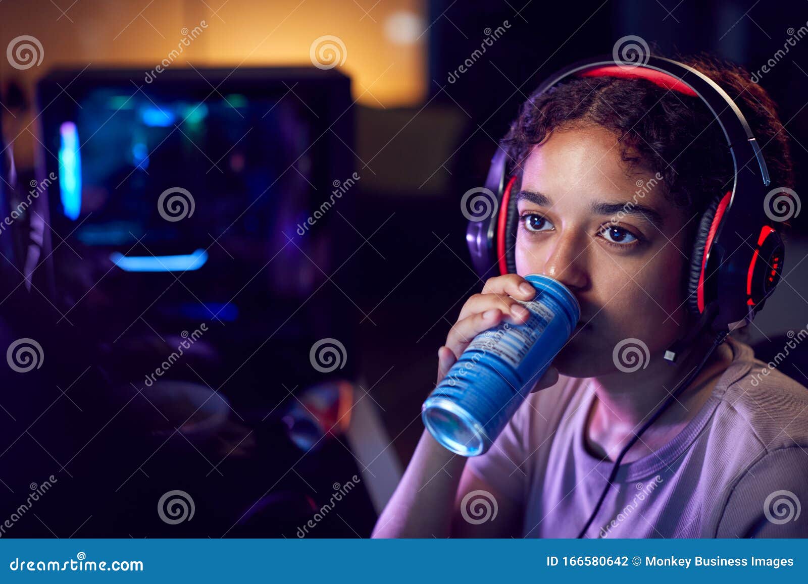 teenage girl drinking caffeine energy drink gaming at home using dual computer screens at night