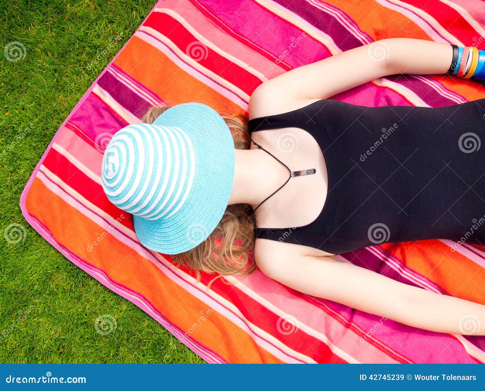 Teenage Girl with a hat covering her face lying on her back on a colorful rug in the grass