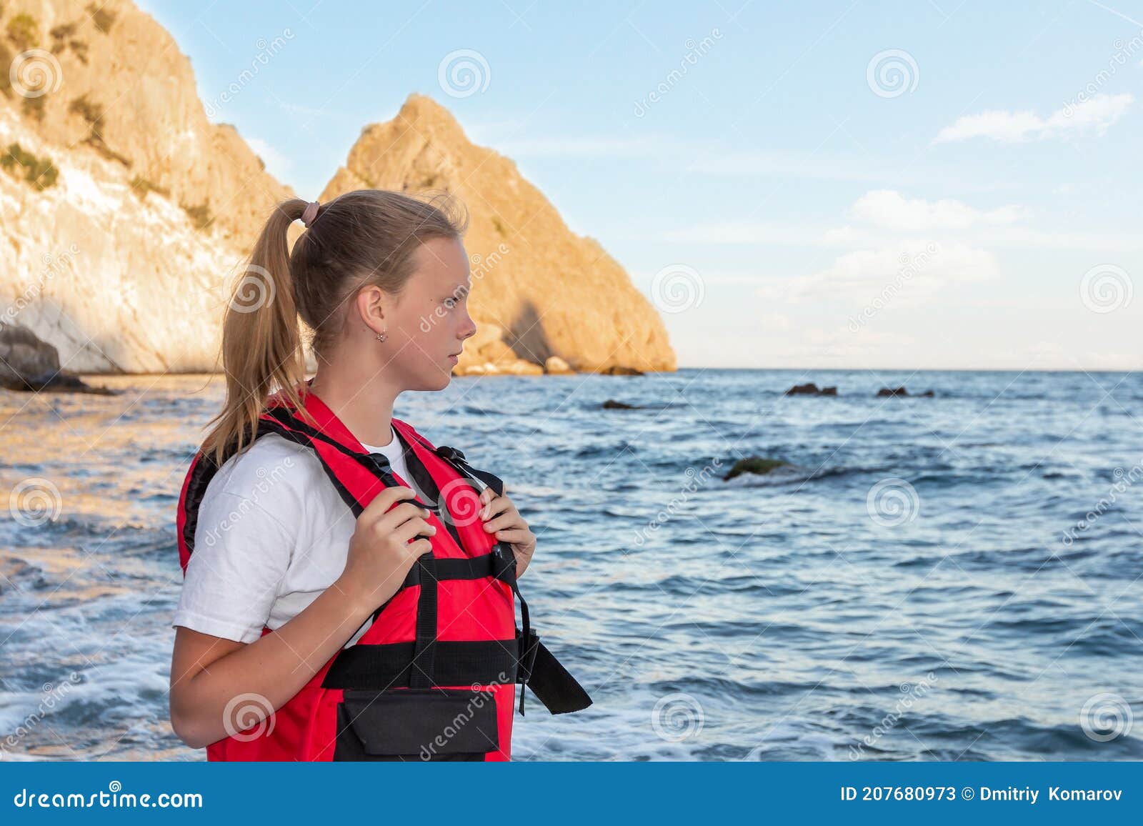 teenage girl in red life jacket stands on ocean and looks at sea. means of rescuing people on water, buoyancy and safety