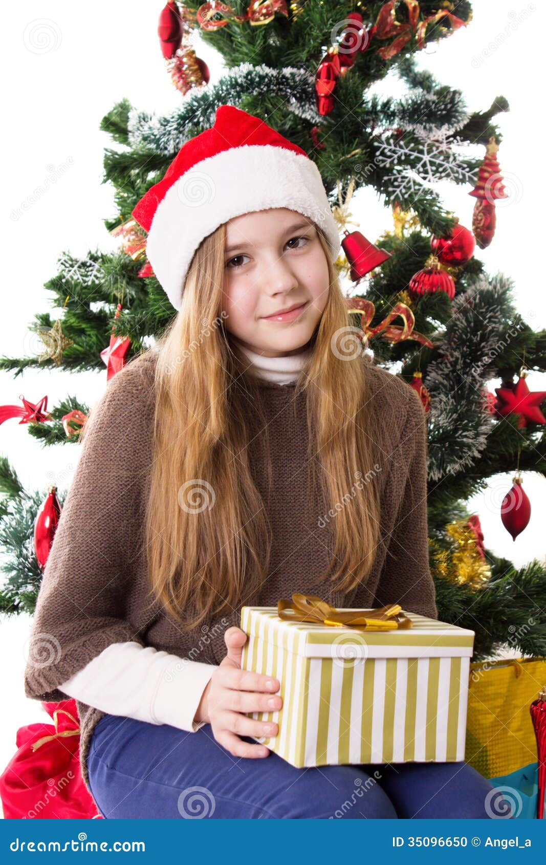 Teenage Girl In Santa Hat With Present Under Christmas Tree Stock Photo