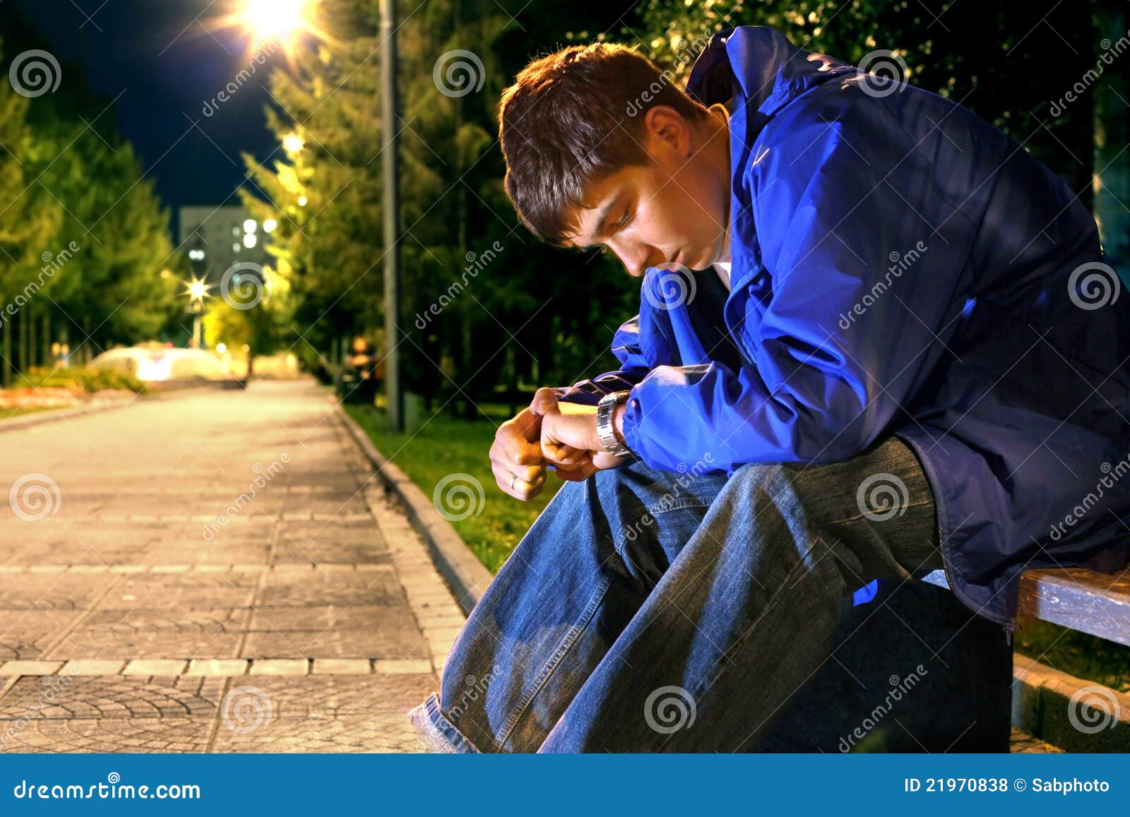 Teenager looking on the watch. Teenager sitting in the night park alley and looking on the watch