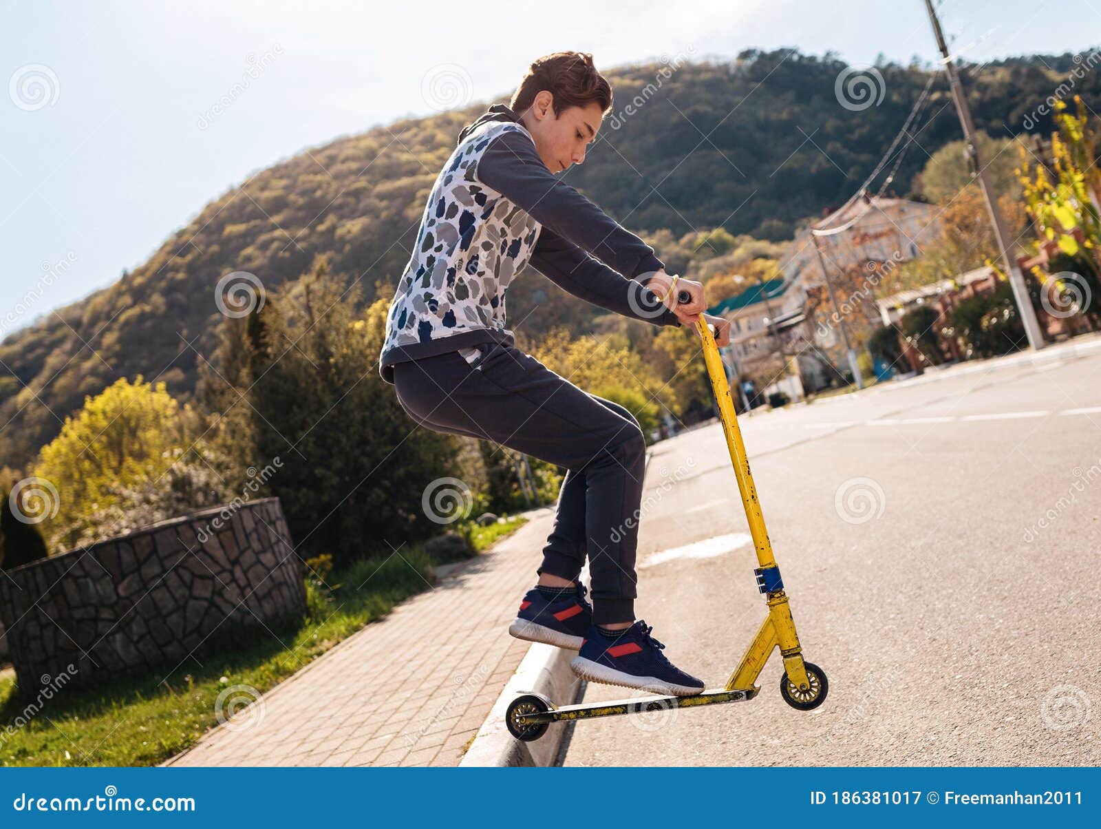 A Teenager Performs a Trick on a Scooter, Jumping Off the Sidewalk on it.  in the Background-an Empty Street and a View of the Stock Image - Image of  leisure, concept: 186381017