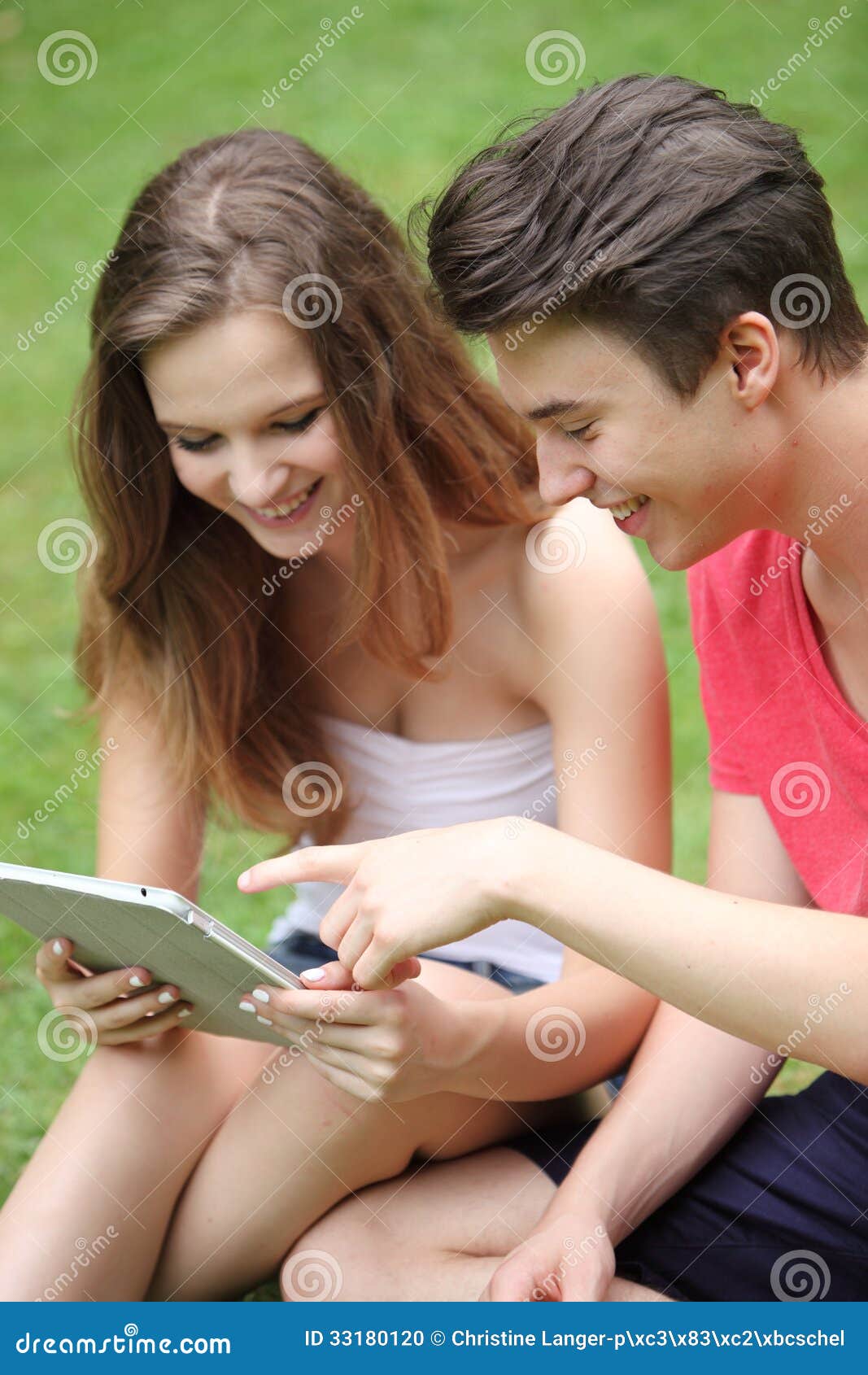 Teenager und Mädchen, das einen TabletpC verwendet. Attraktiver entspannter glücklicher junger Teenager und Mädchen, die auf grünem Gras unter Verwendung eines TabletpC sitzt