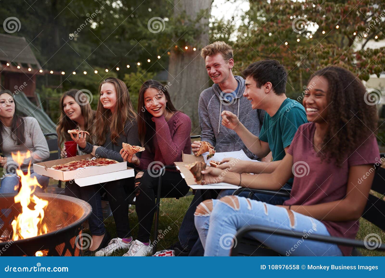 teenagers at a fire pit eating take-away pizzas, close up