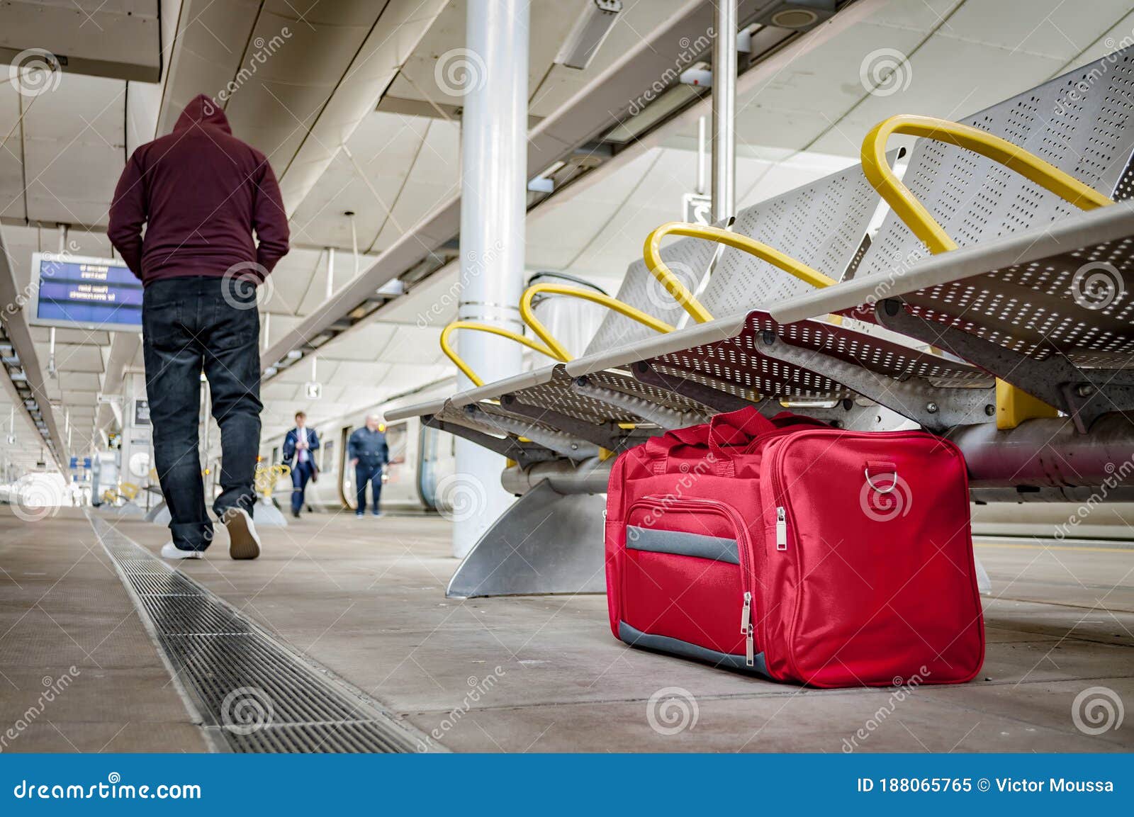 terrorism and public safety concept with an unattended bag left under chair on platform at train station or airport and man