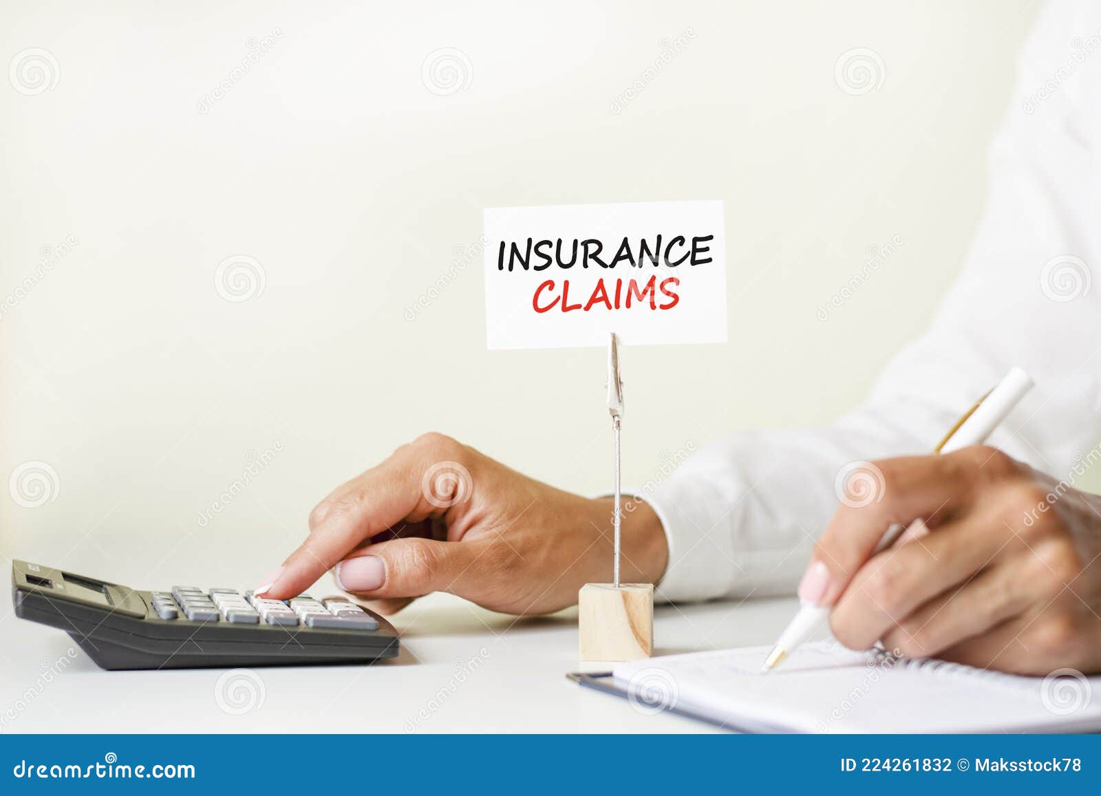 the text insurance claims written on a white paper card clamped in a paper holder. in the background woman`s hands writing with