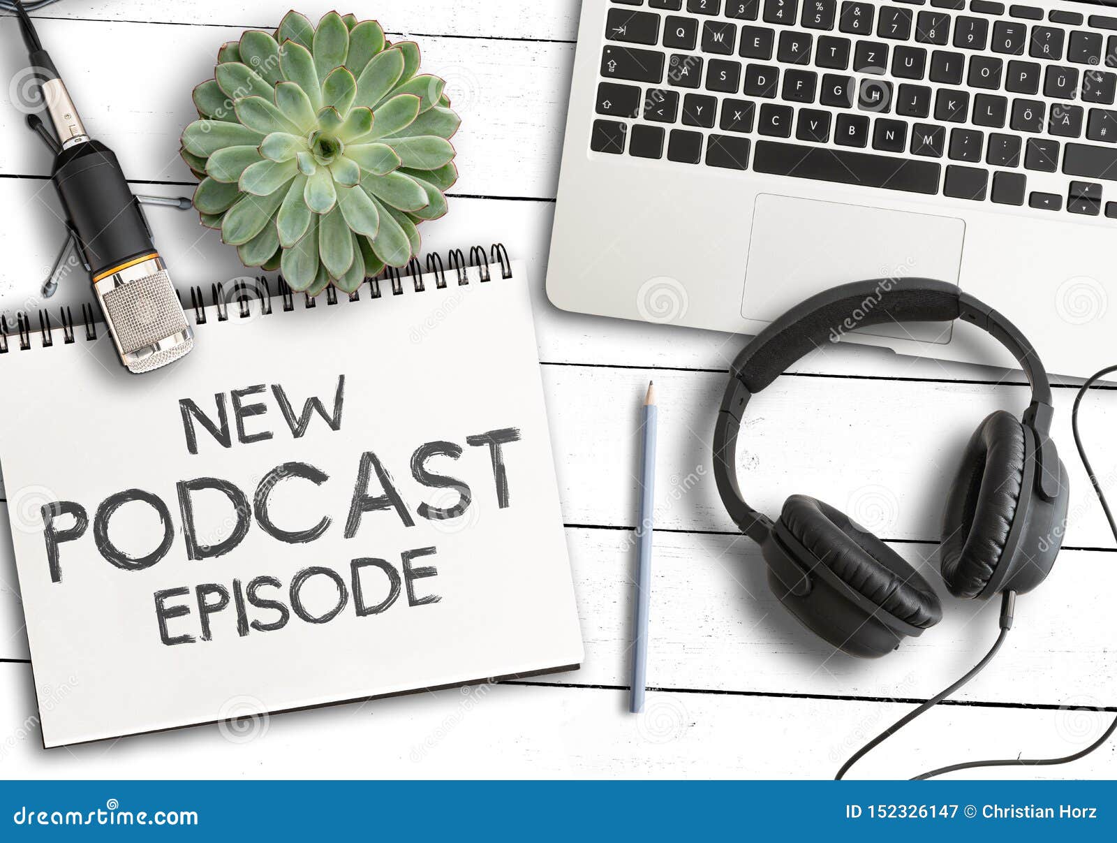 text new podcast episode on notepad with laptop computer, potted plant and recording microphone on white wooden table