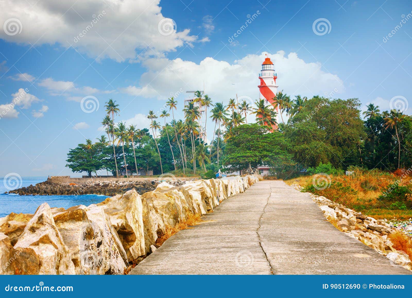 thangassery lighthouse on the cliff surrounded by palm trees and big sea waves on the kollam beach. kerala, india