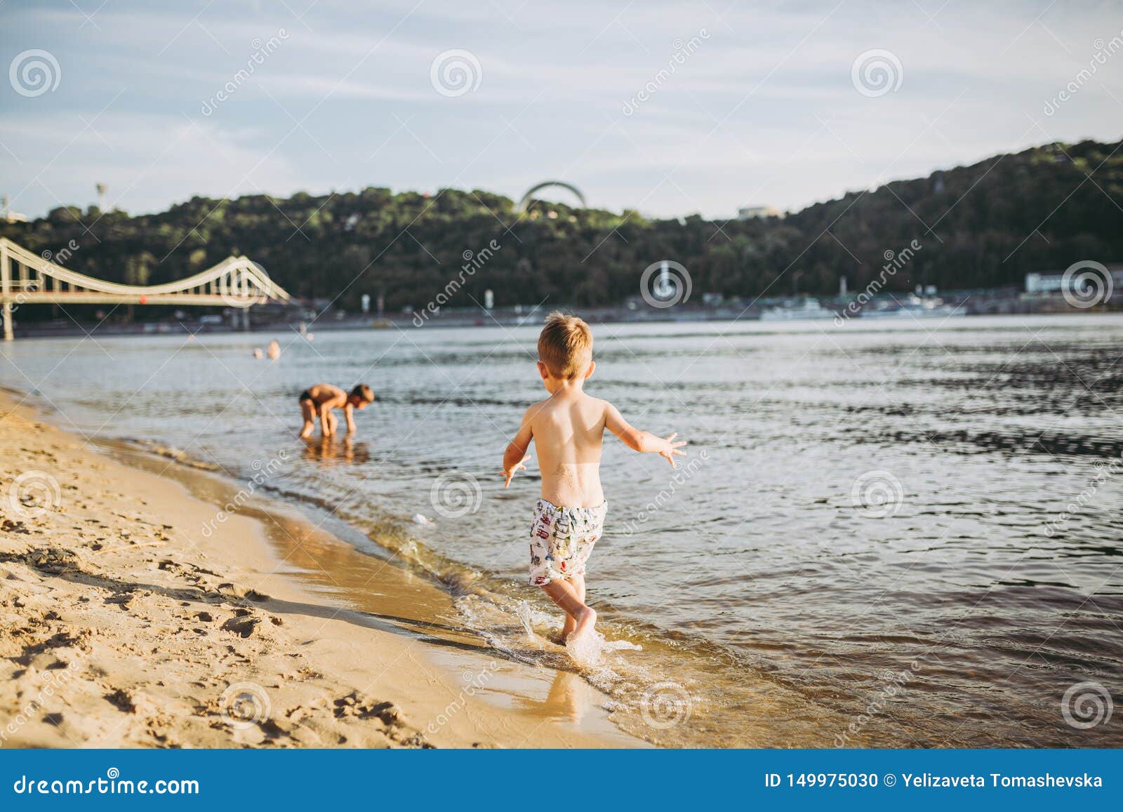 theme summer outdoor activities near the river on the city beach in kiev ukraine. little funny baby boy running along the river