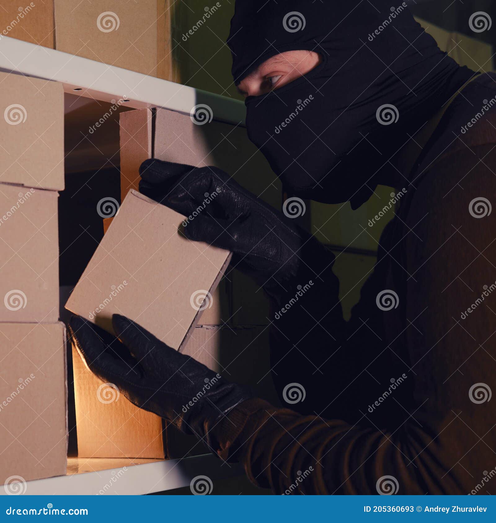 A Thief in a Black Hood Steals a Parcel in a Warehouse in the Dark