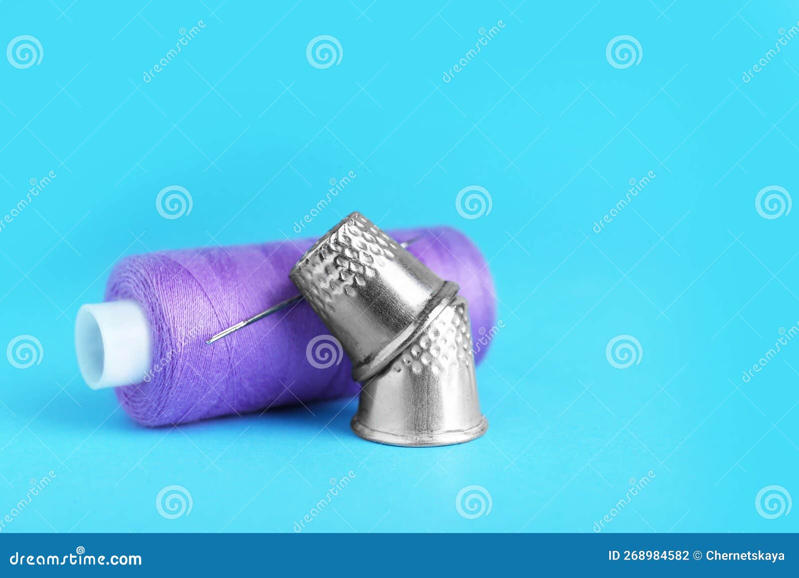 Thimbles and Spool of Purple Sewing Thread with Needle on Light Blue