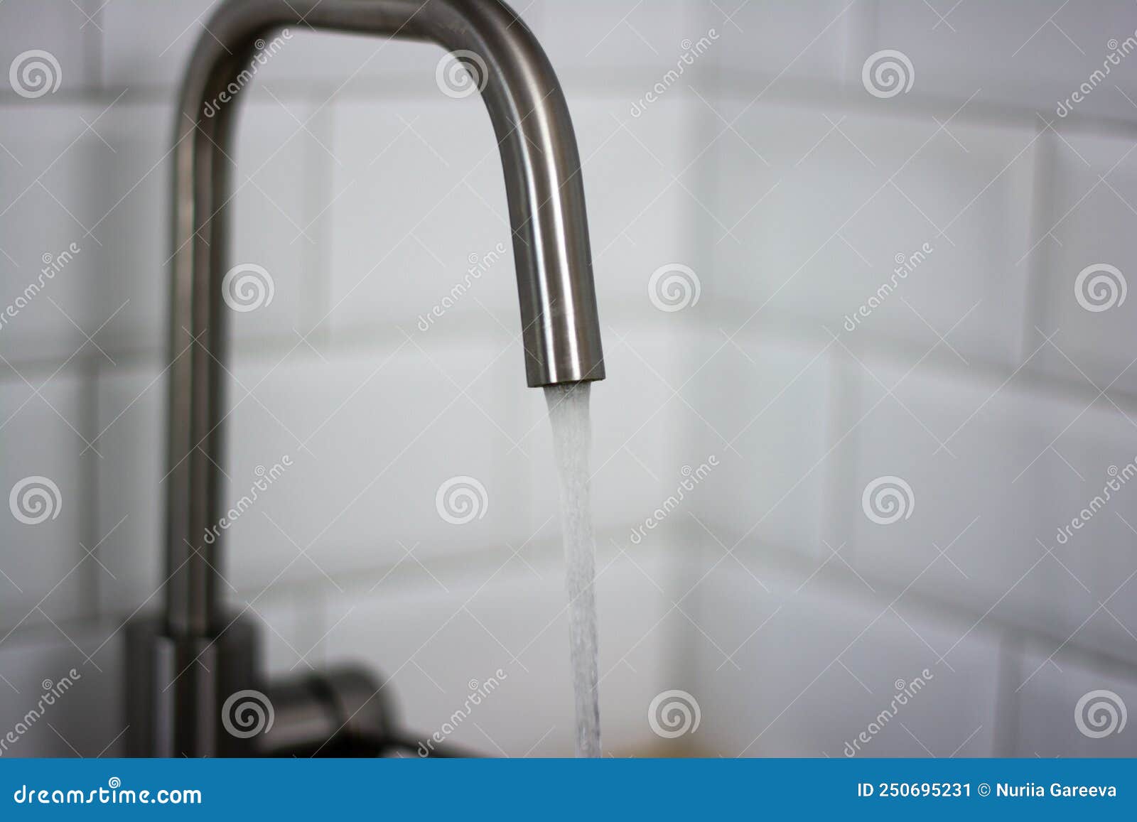 Thin Stream of Water Flowing from the Tap Against a White Tile in the