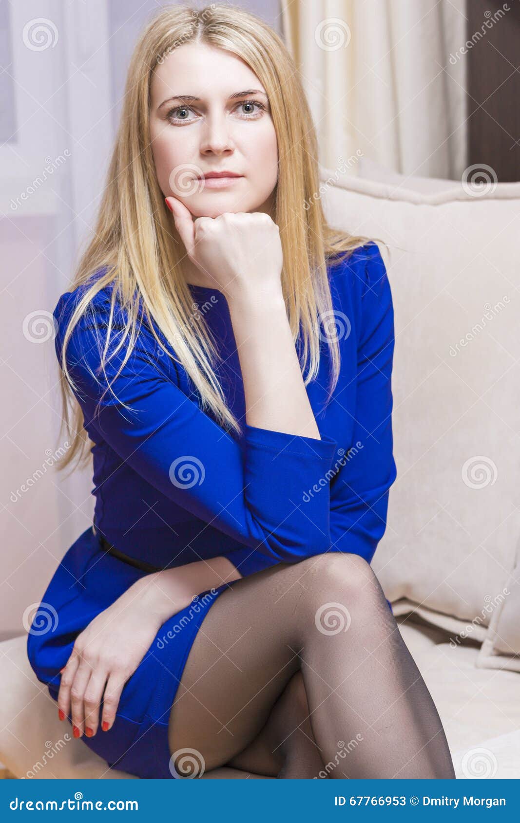 Thoughtful Blond Caucasian Female in Blue Dress Sitting on Couch Stock ...