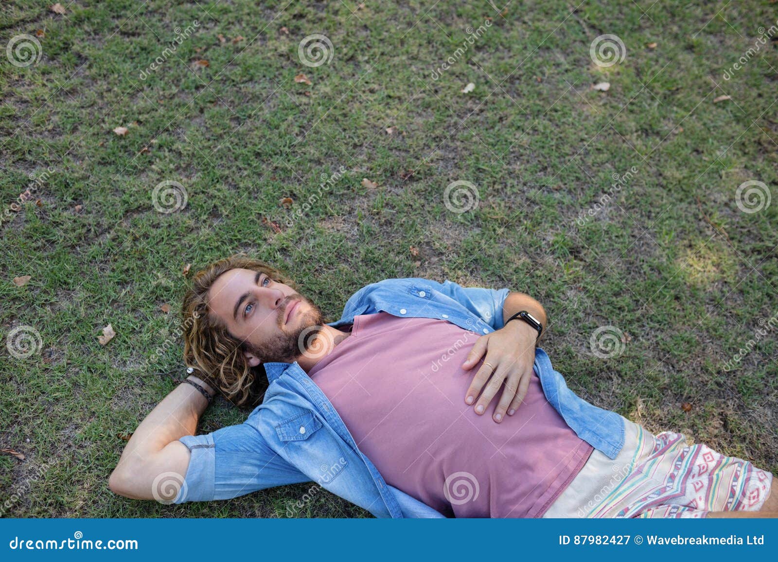 thoughtful man lying on grass with hand behind head