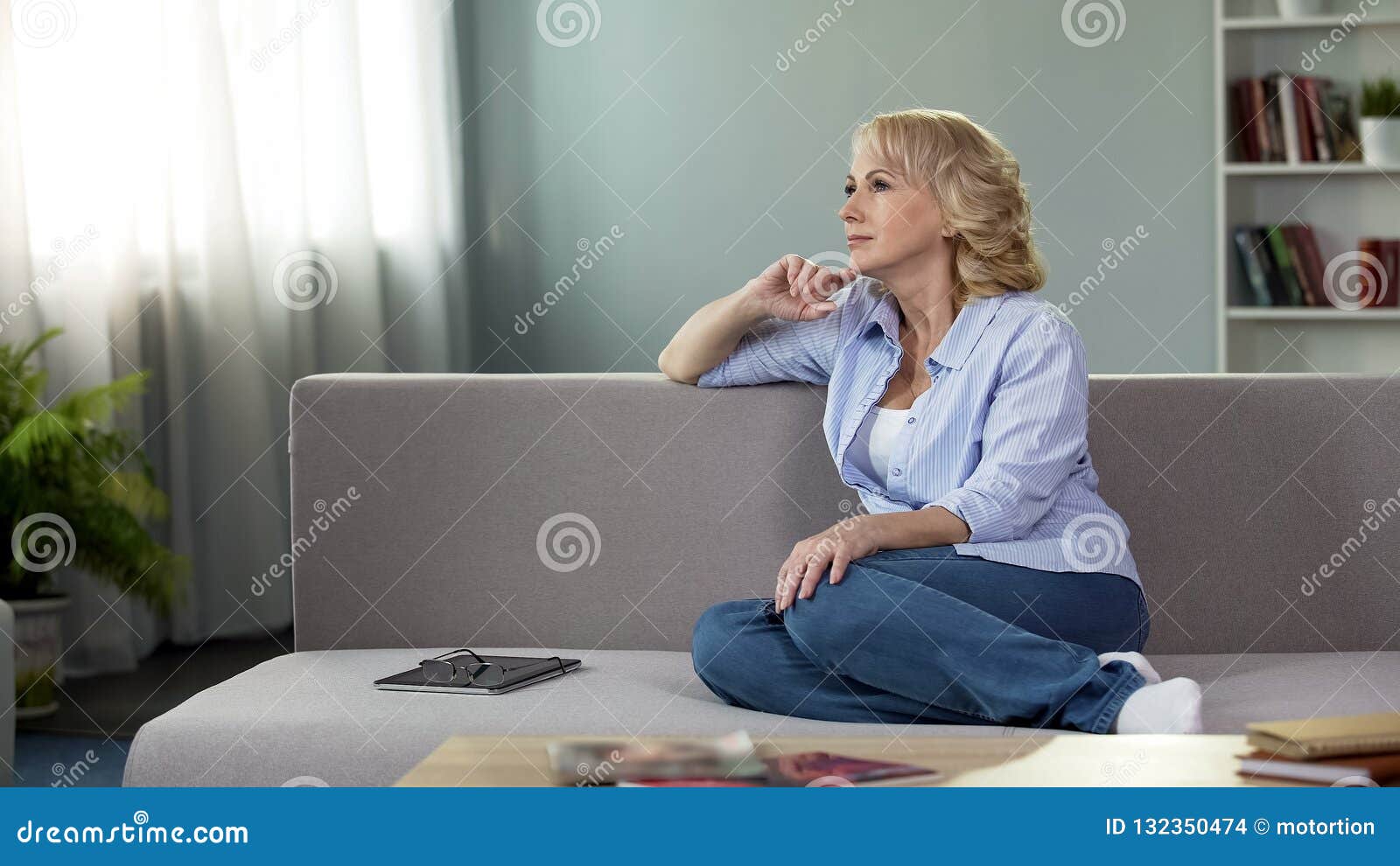 thoughtful pretty woman relaxing on sofa at home, free time retirement, leisure