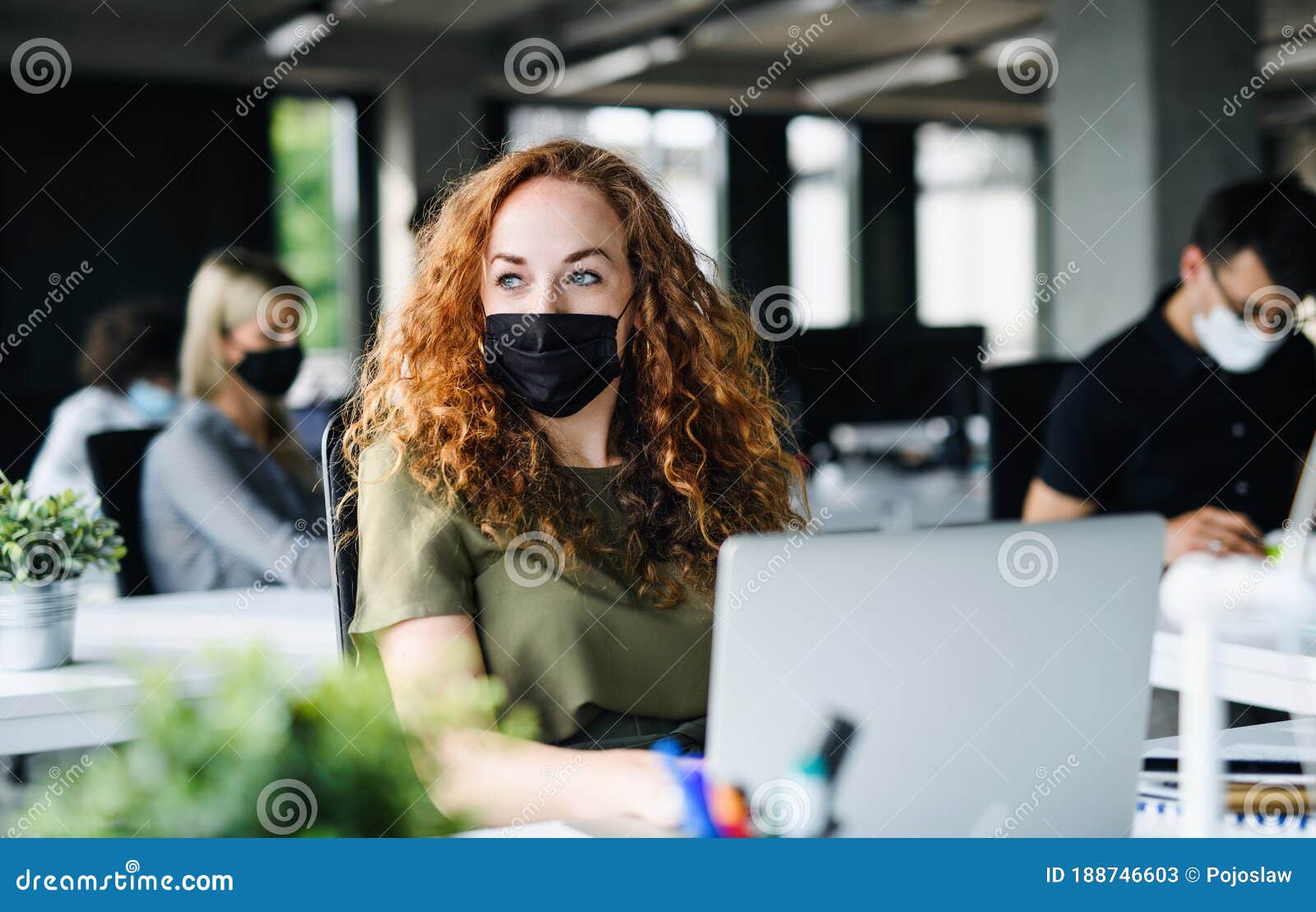 young woman with face mask back at work in office after lockdown.