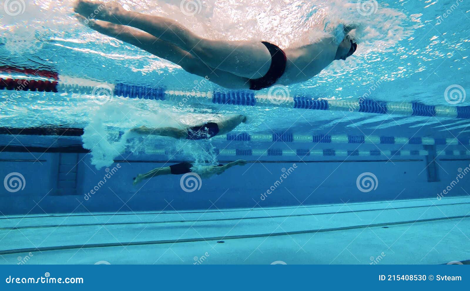 Three Athletes Swim Underwater Using Dolphin Kick Technique Stock