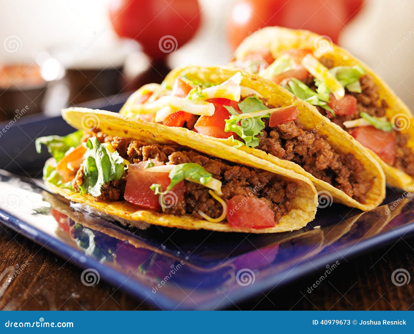 three beef tacos with cheese, lettuce and tomatoes