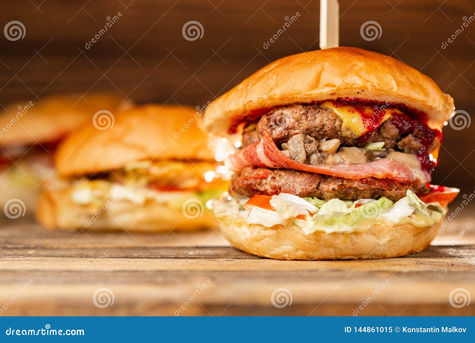 three big burger with meat cooked on bbq coal. lunch on a wooden background. the concept of fast food and unhealthy food