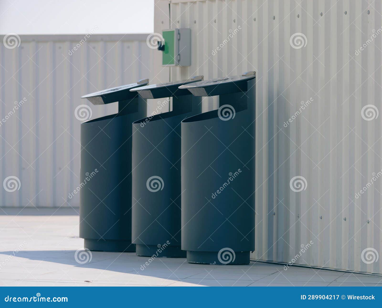 Three Black Plastic Trash Cans Lined Up Sidebyside Against a White