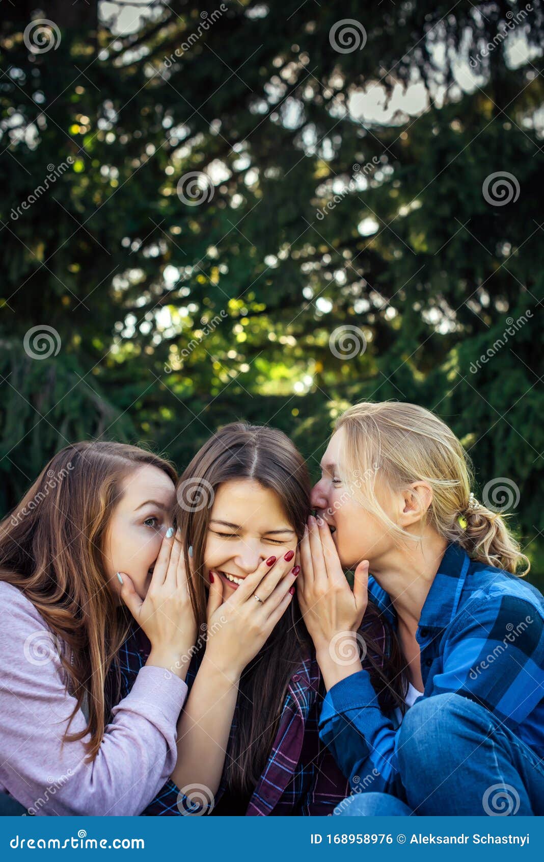 Three Cheerful Girls Whisper And Gossip Against Green Foliage In The Park Women Joke And Laugh