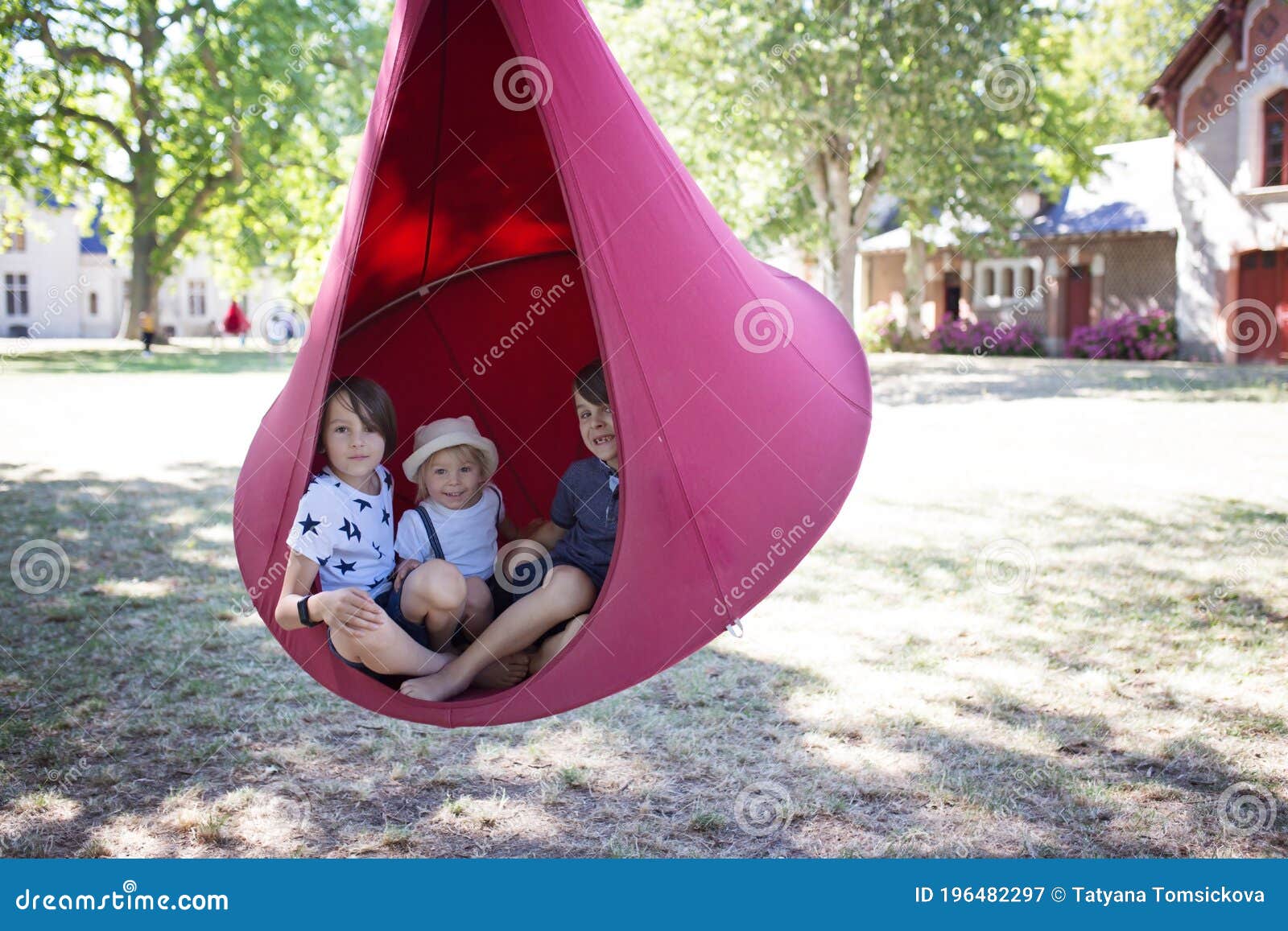 three children, boys swinging in a big cloth swing in a park