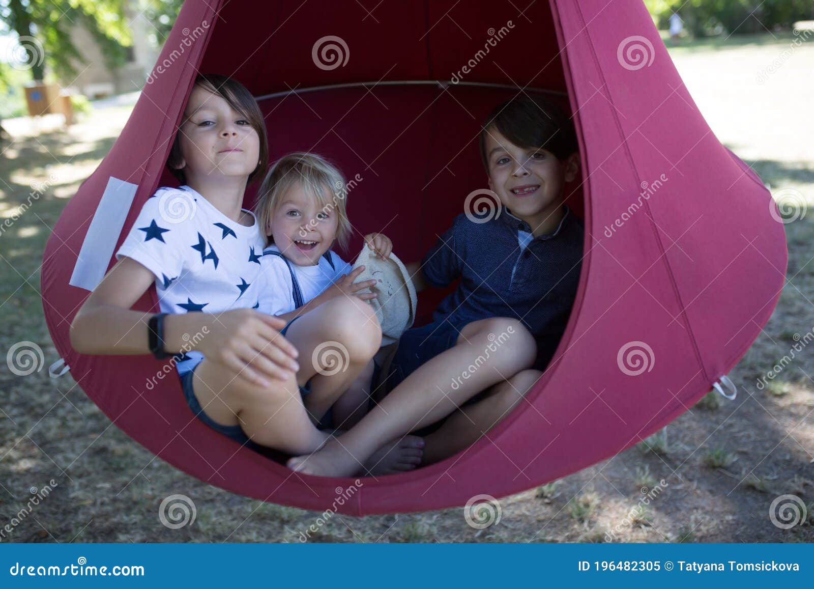 three children, boys swinging in a big cloth swing in a park