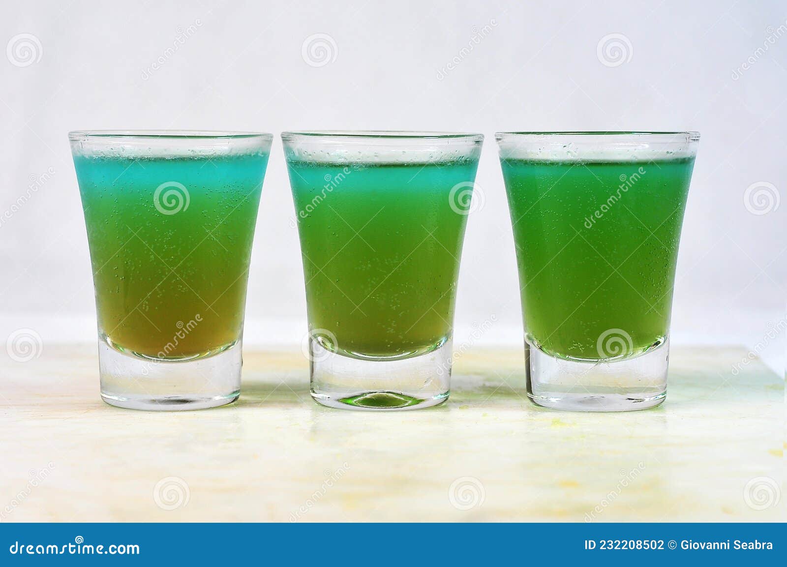 three drink dose of absinthe, tequila and vodka with lemon in the glass cup on the table, horizontal image with blurred background