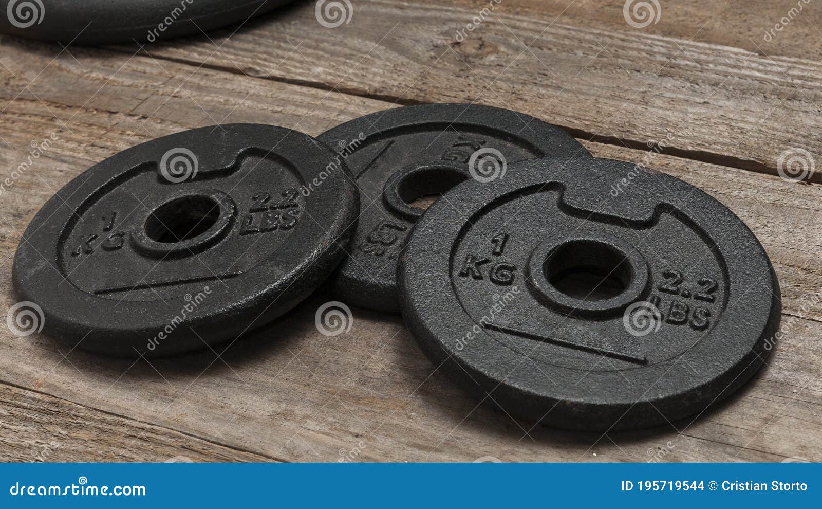 Three Dumbbell Discs For Weight Lifting On Wooden Floor Stock Photo