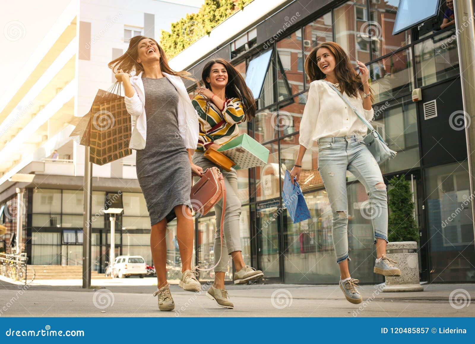 three fashionable young women strolling with shopping bags. satisfied women jumping on street.