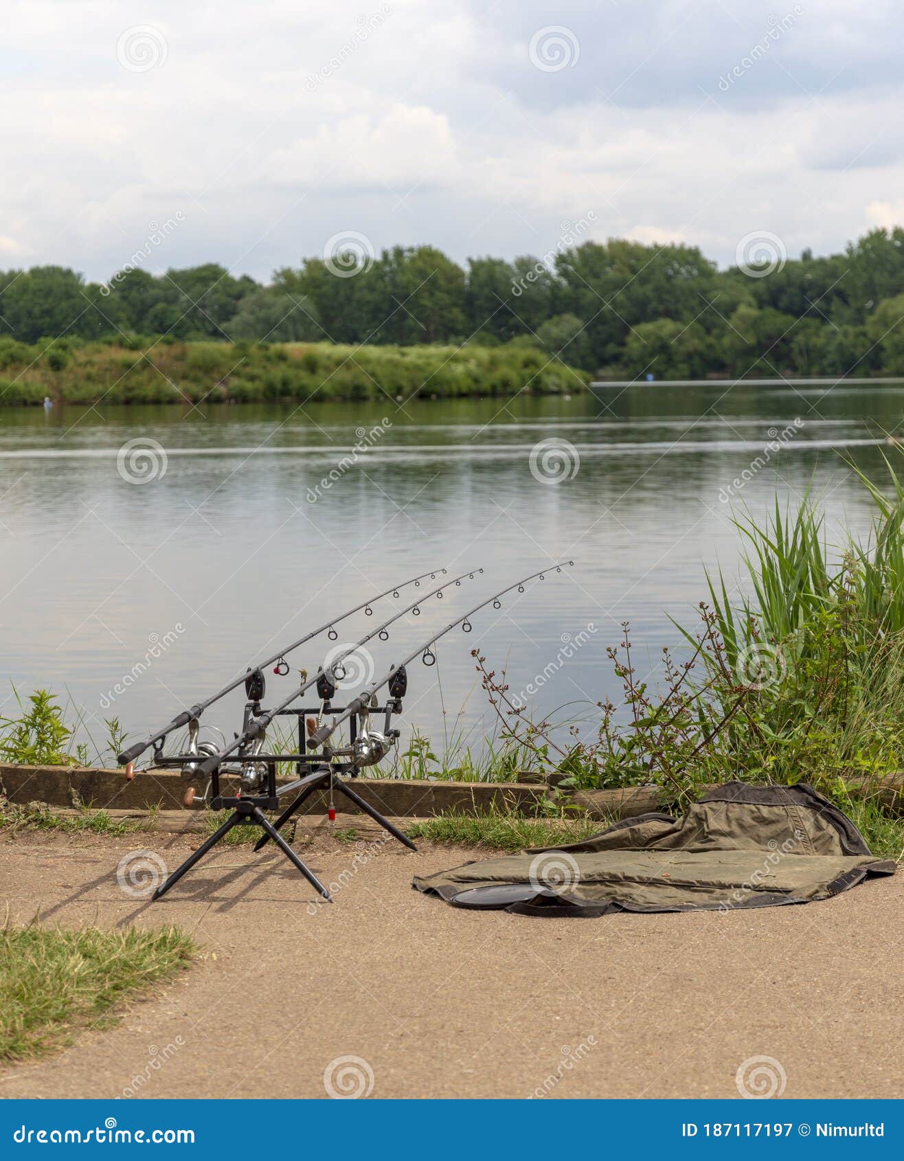 Three Fishing Rods with Reels at the Side of a Peaceful Lake Stock