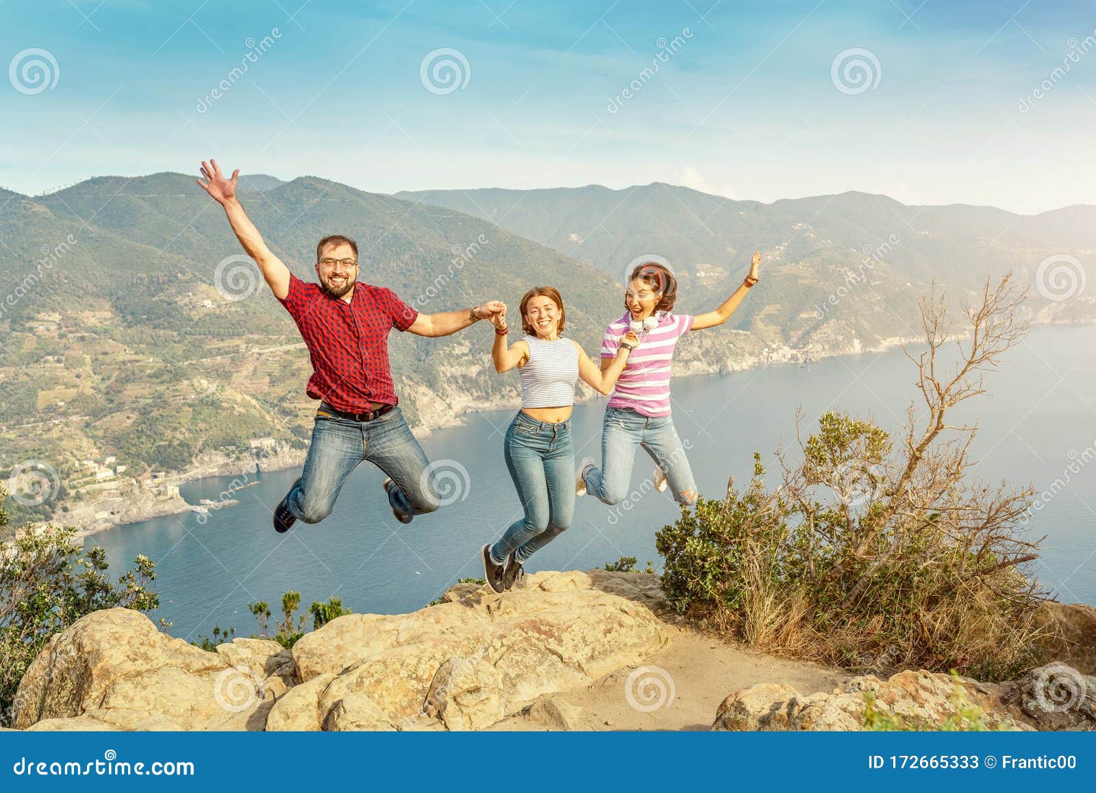 three friends jumping and having fun at the seaside resort in the cinque tere nature park in italy