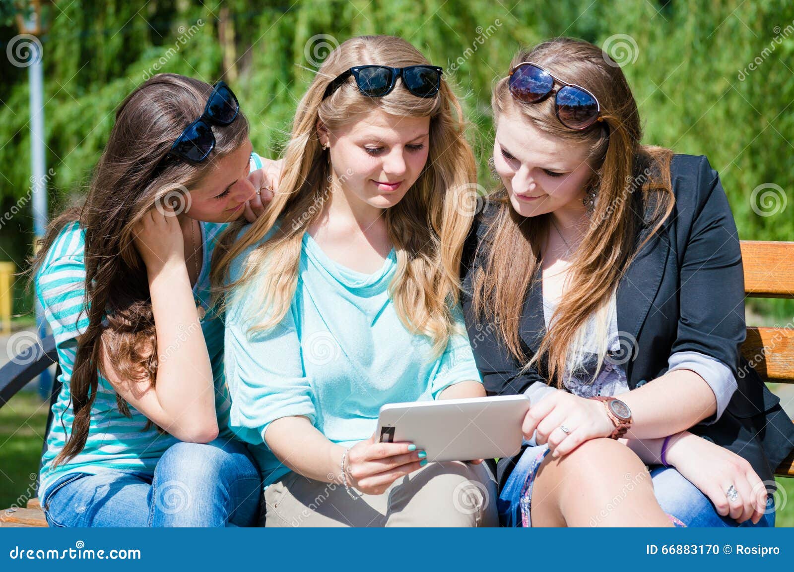 Three Friends Sitting in Park and Looking Something on Tablet Stock ...