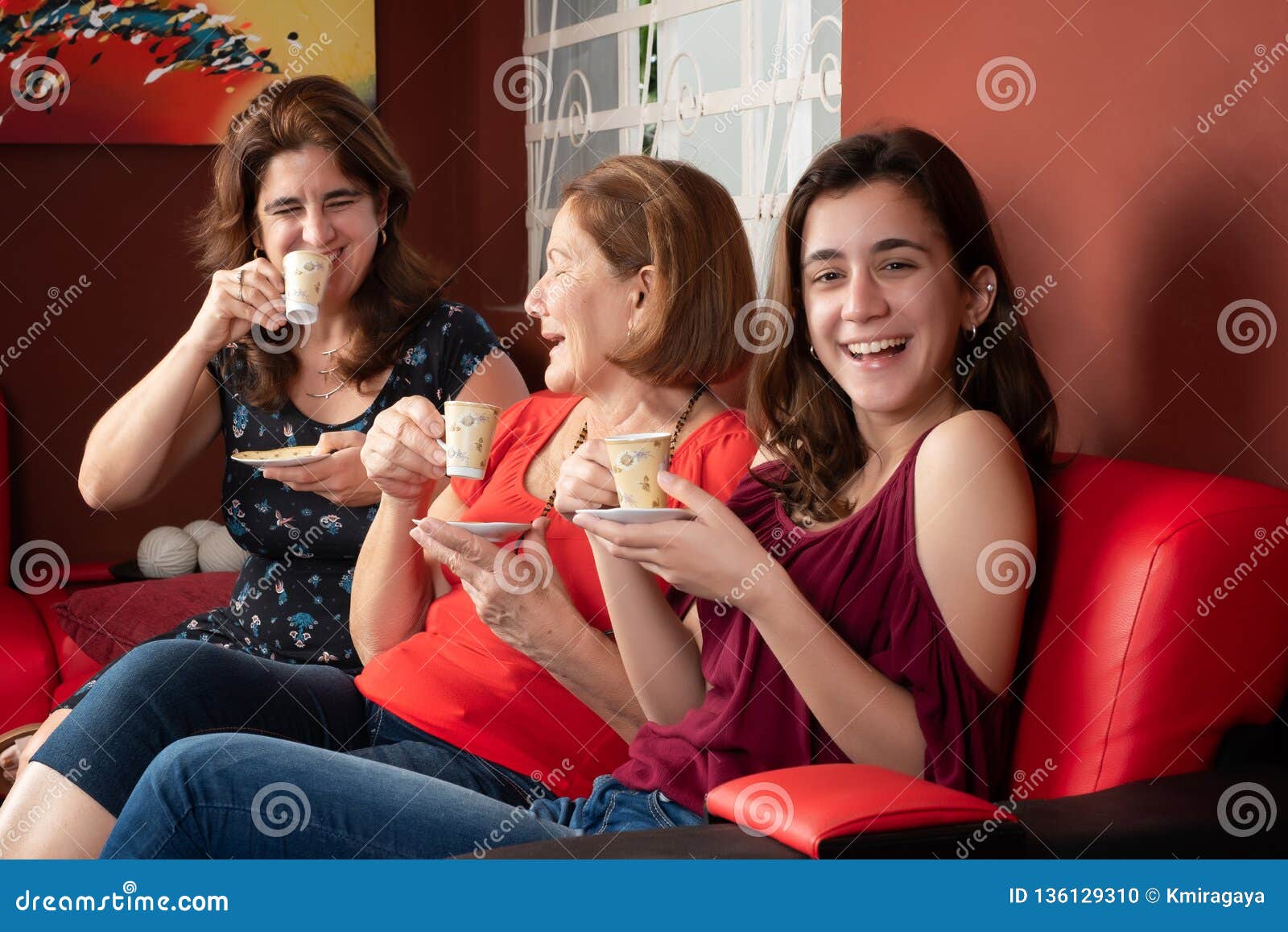 three generations of hispanic women laughing and drinking coffee