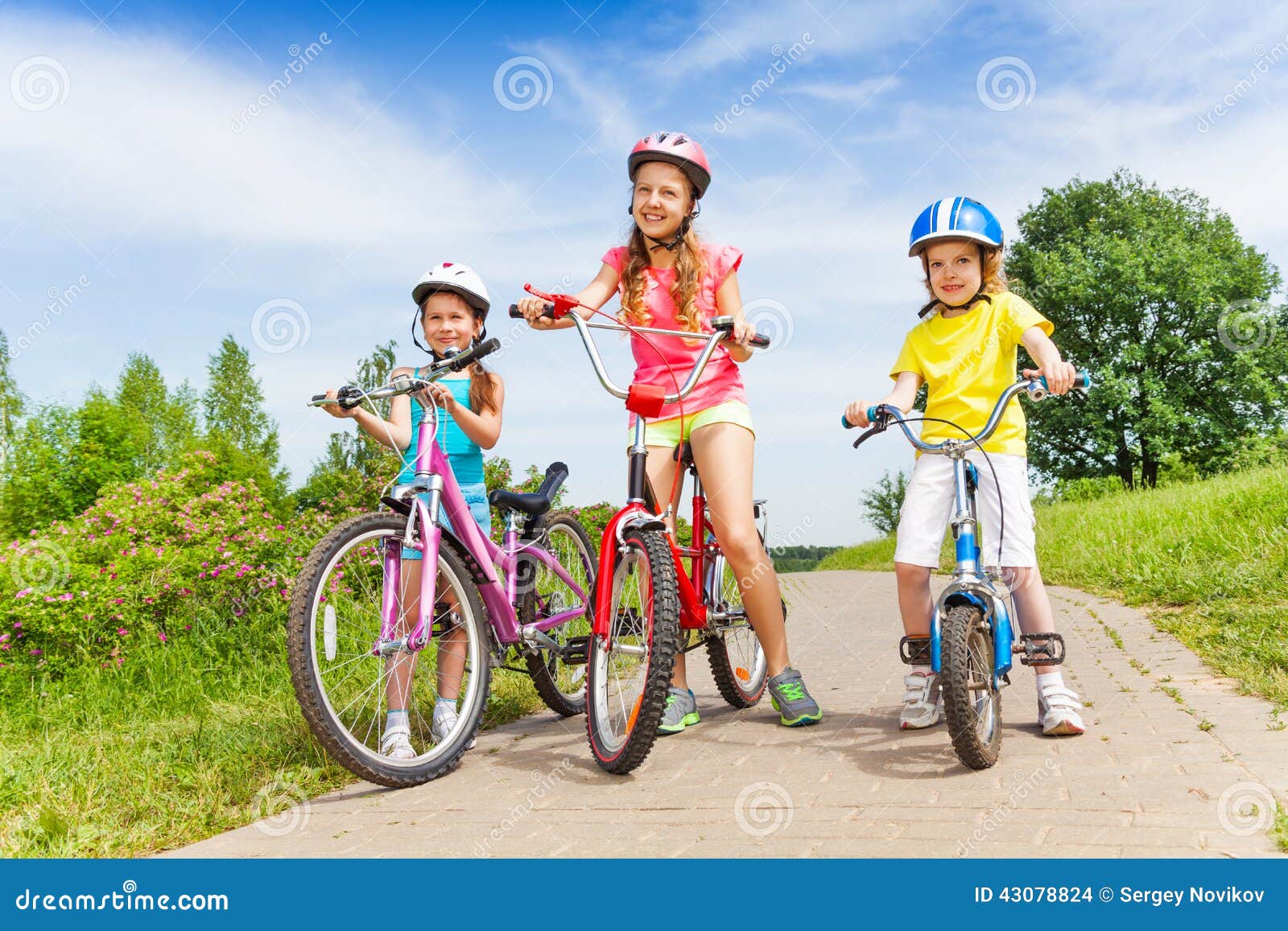 three girls on a pave road with bicycles