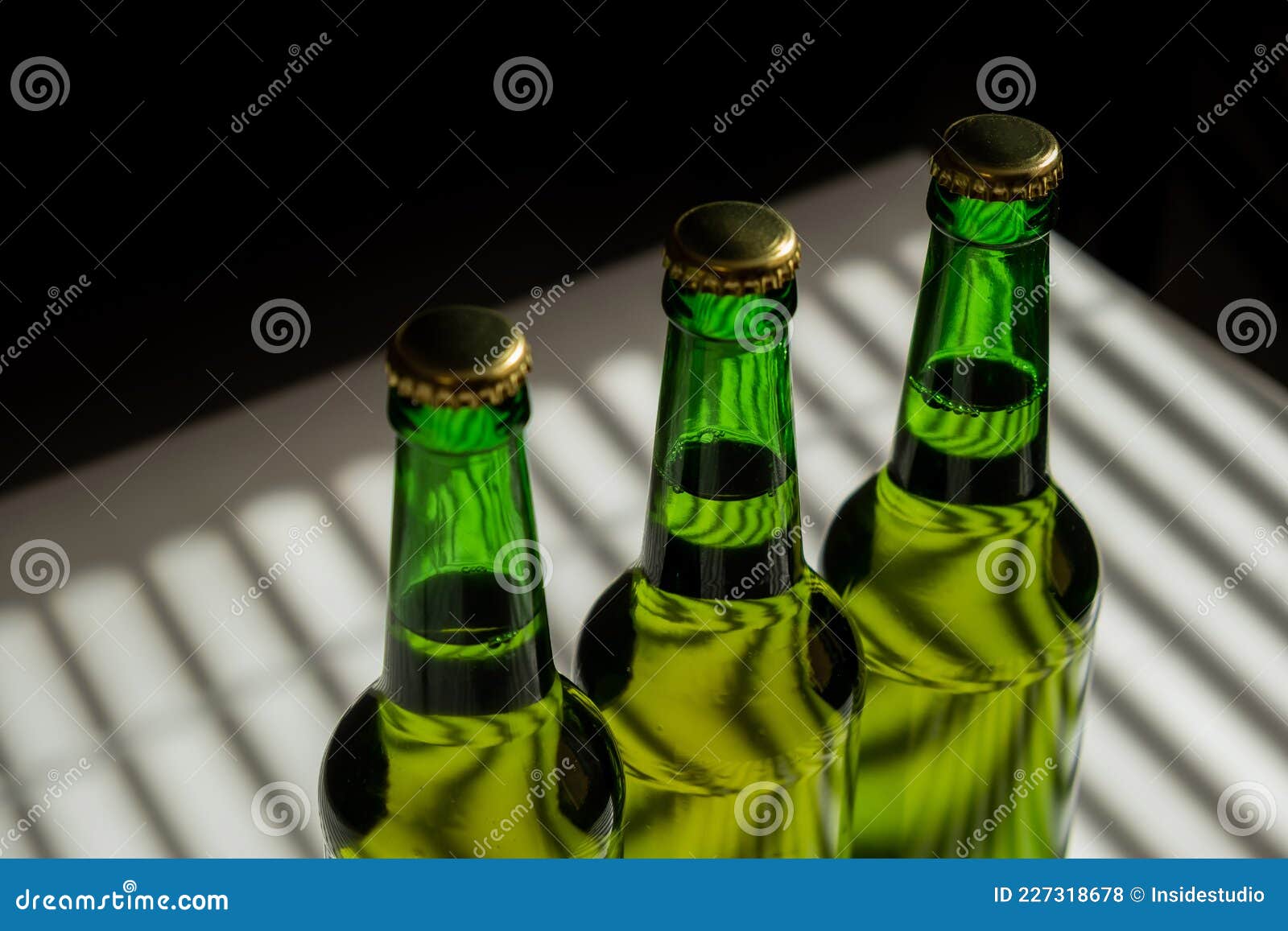 Three Green Glass Beer Bottles in the Shade of the Blinds. Stock Photo