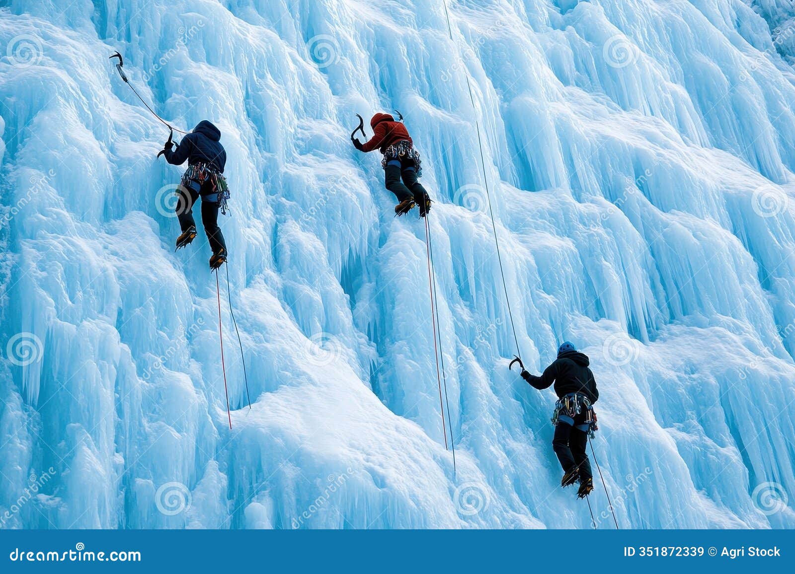 three ice climbers ascending a frozen waterfall