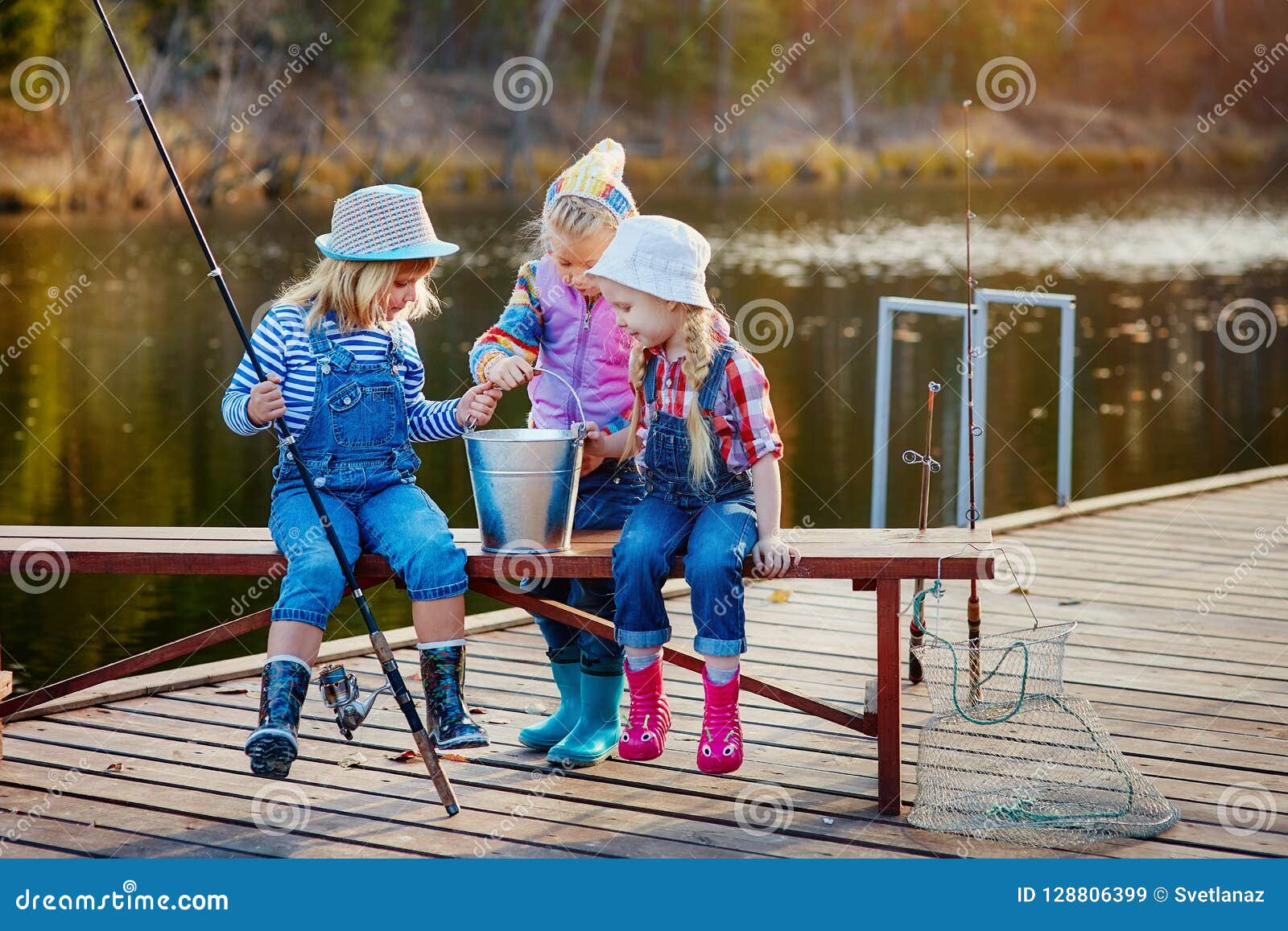 Two little girls with fishing rods, sitting on a wooden pontoon and  bragging of caught fish Stock Photo