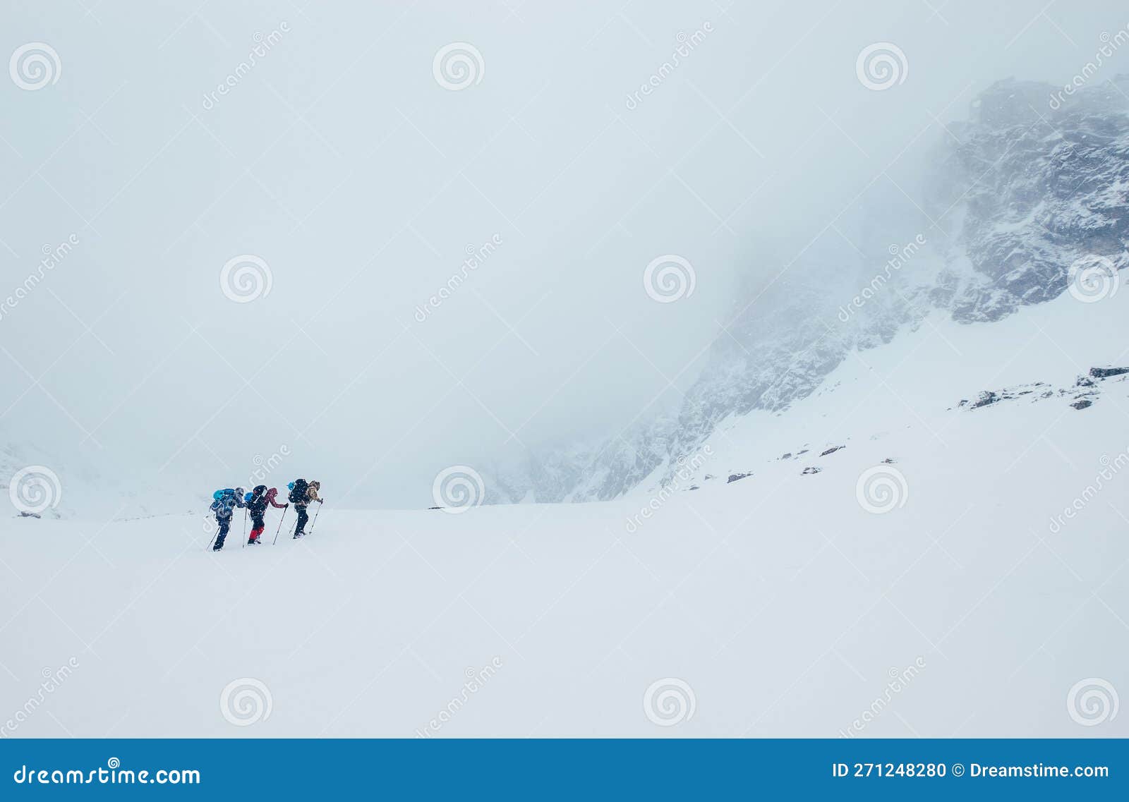 three members rope team ascending the high mountain winter peak. blizard covering the structural basin in vysoke tatry (high