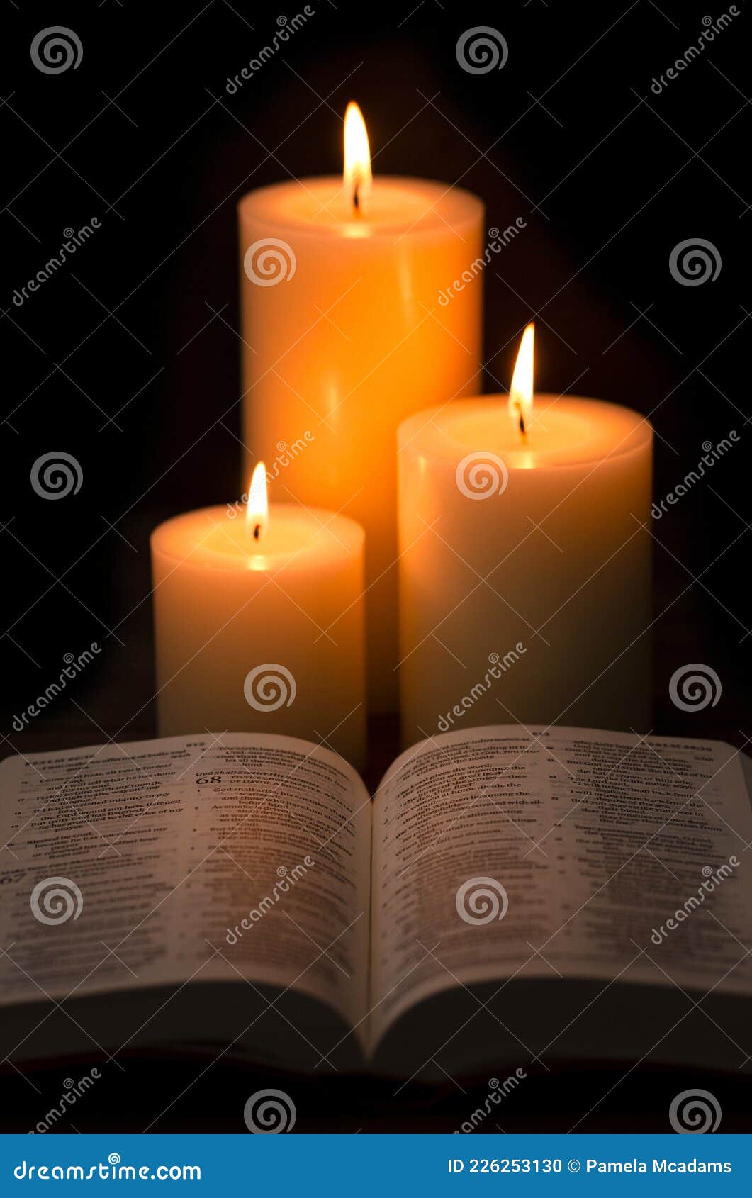 Three Pillar Candles Burning in a Dark Room with a Bible Stock Photo