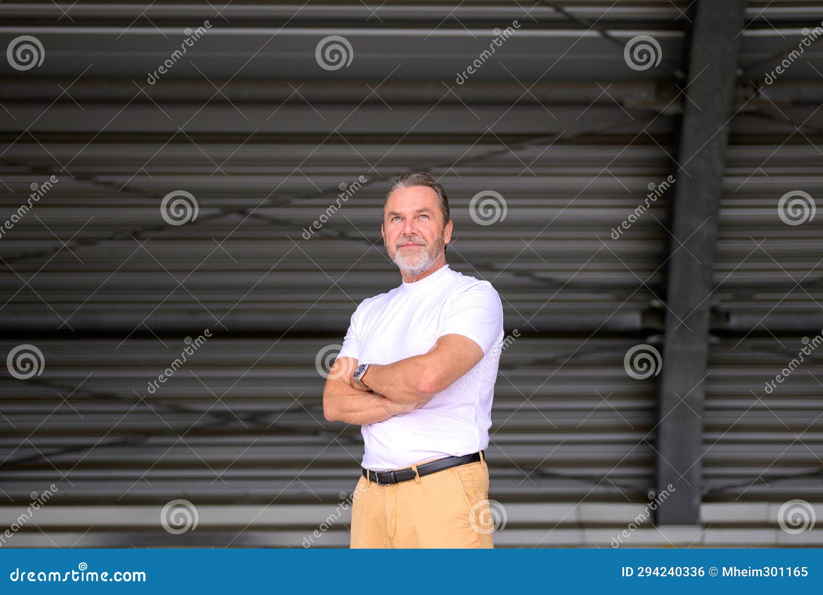 three-quarter body portrait of a man with his arms crossed and looks friendly up