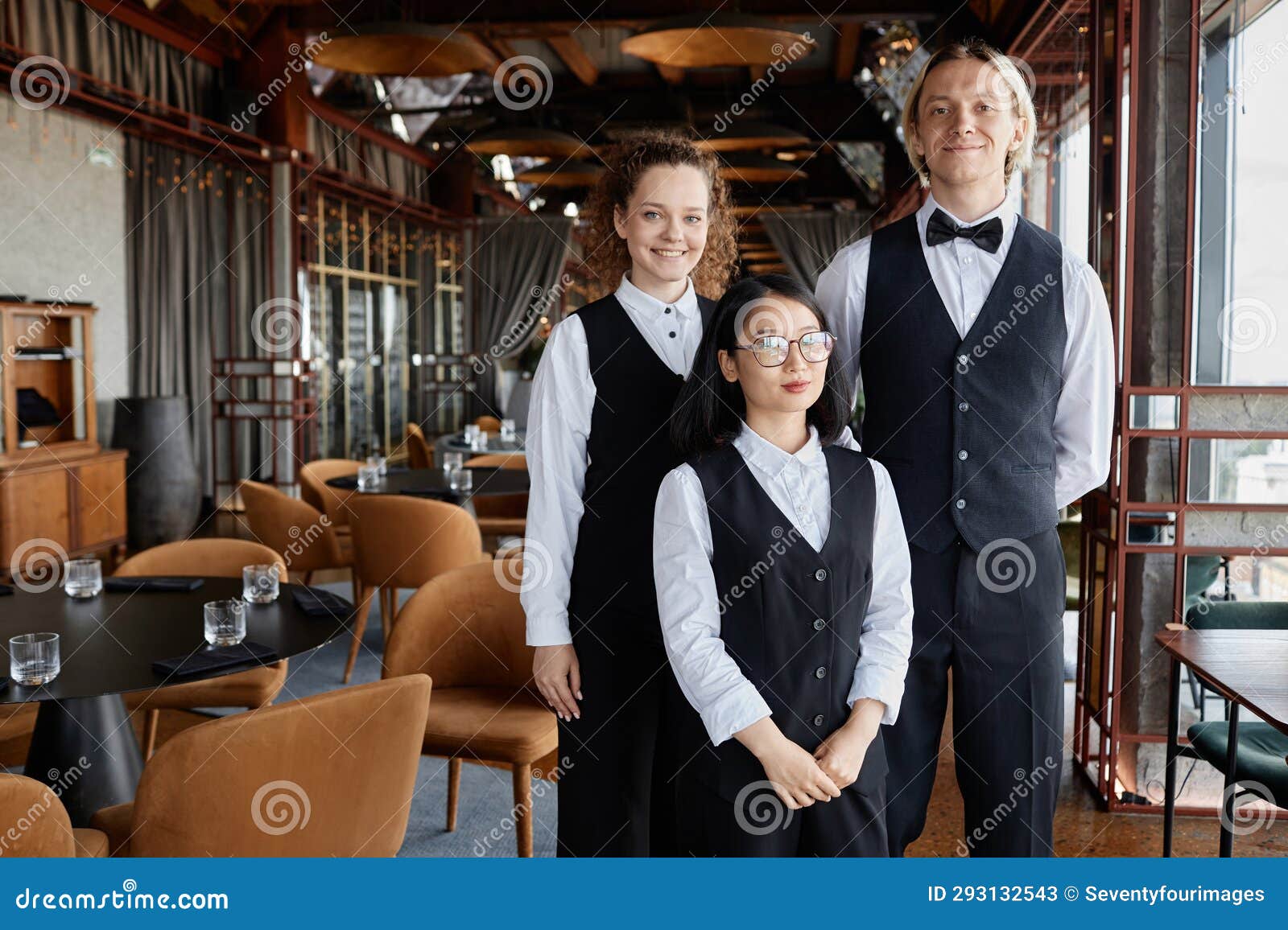 Three Servers Wearing Classic Uniform in Restaurant and Looking at